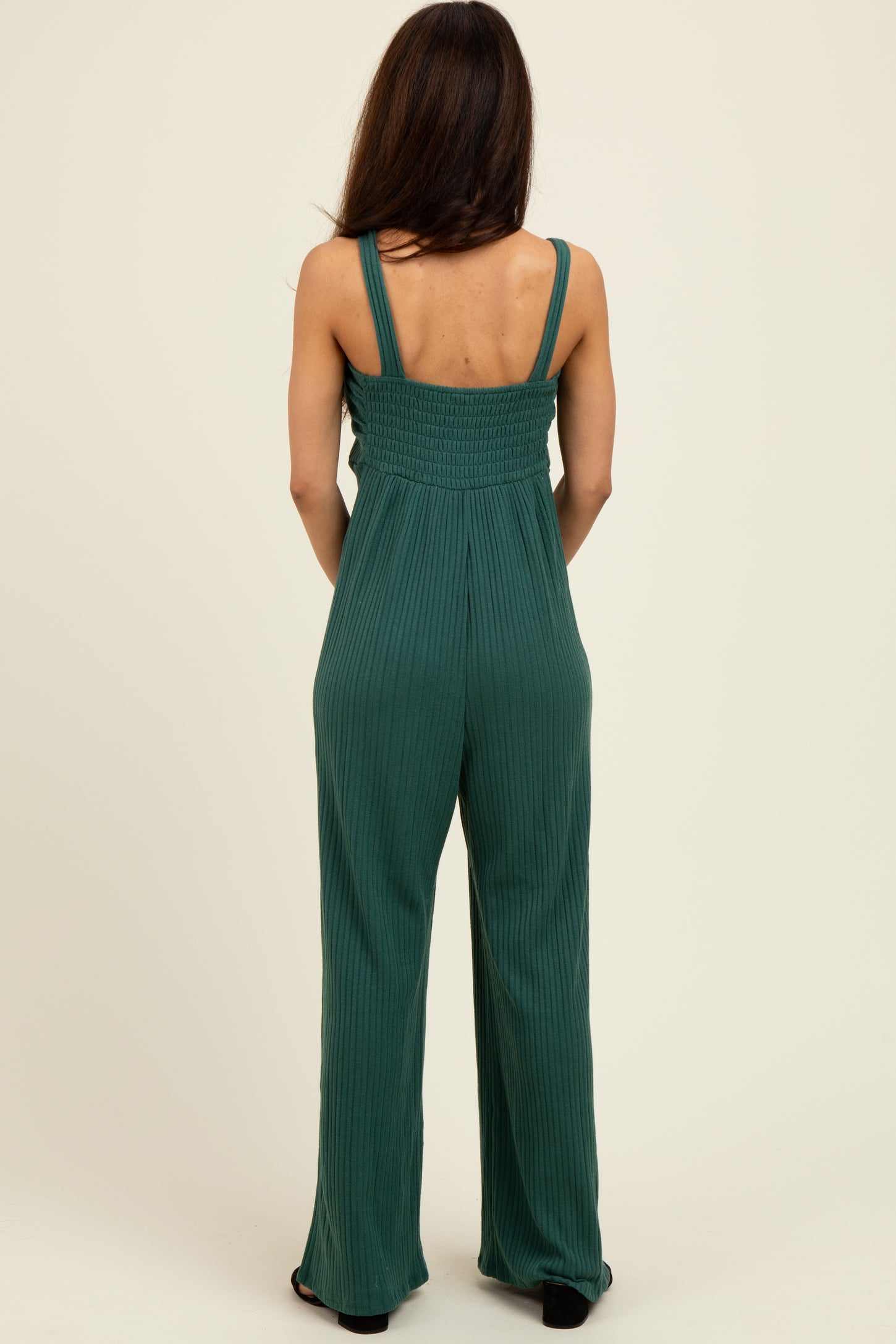 woman wearing a back view of a green ribbed jumpsuit with adjustable straps and wide-leg silhouette