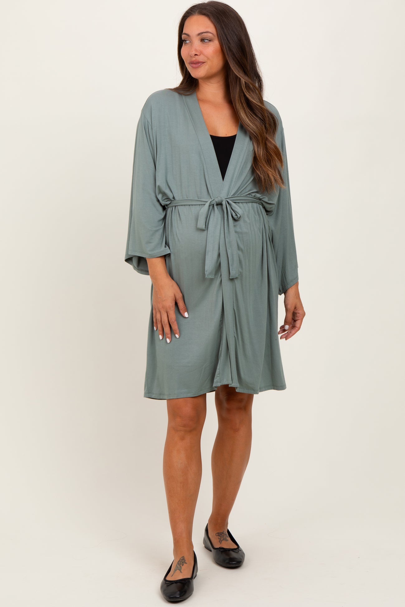 woman wearing a sage green maternity wrap dress with a tie waist and flowing sleeves, showing her baby bump