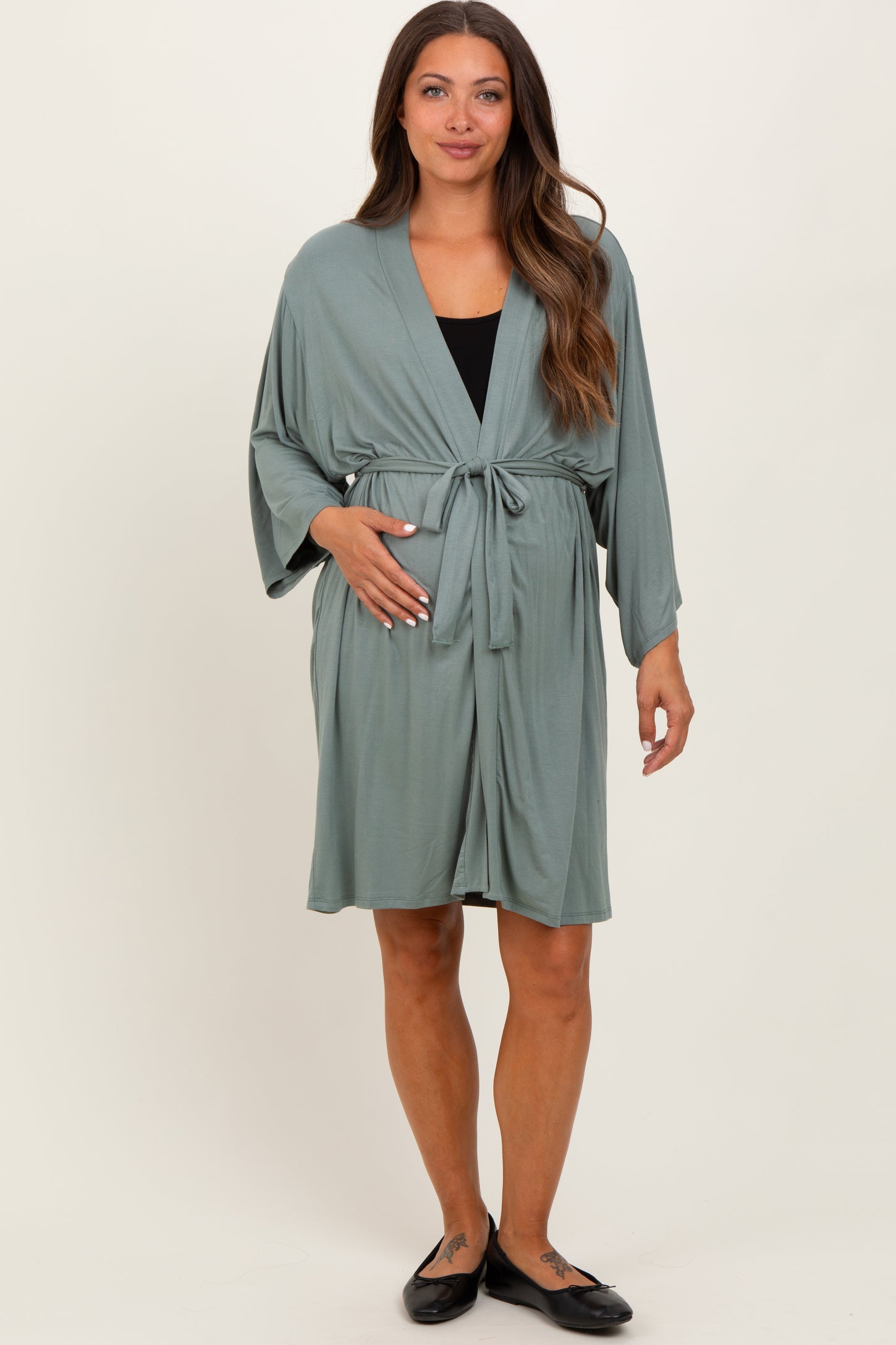 woman wearing a sage green maternity robe with a tie waist, gently holding her baby bump