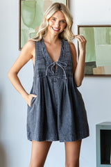 woman wearing a dark denim sleeveless babydoll dress with a tie detail and pockets