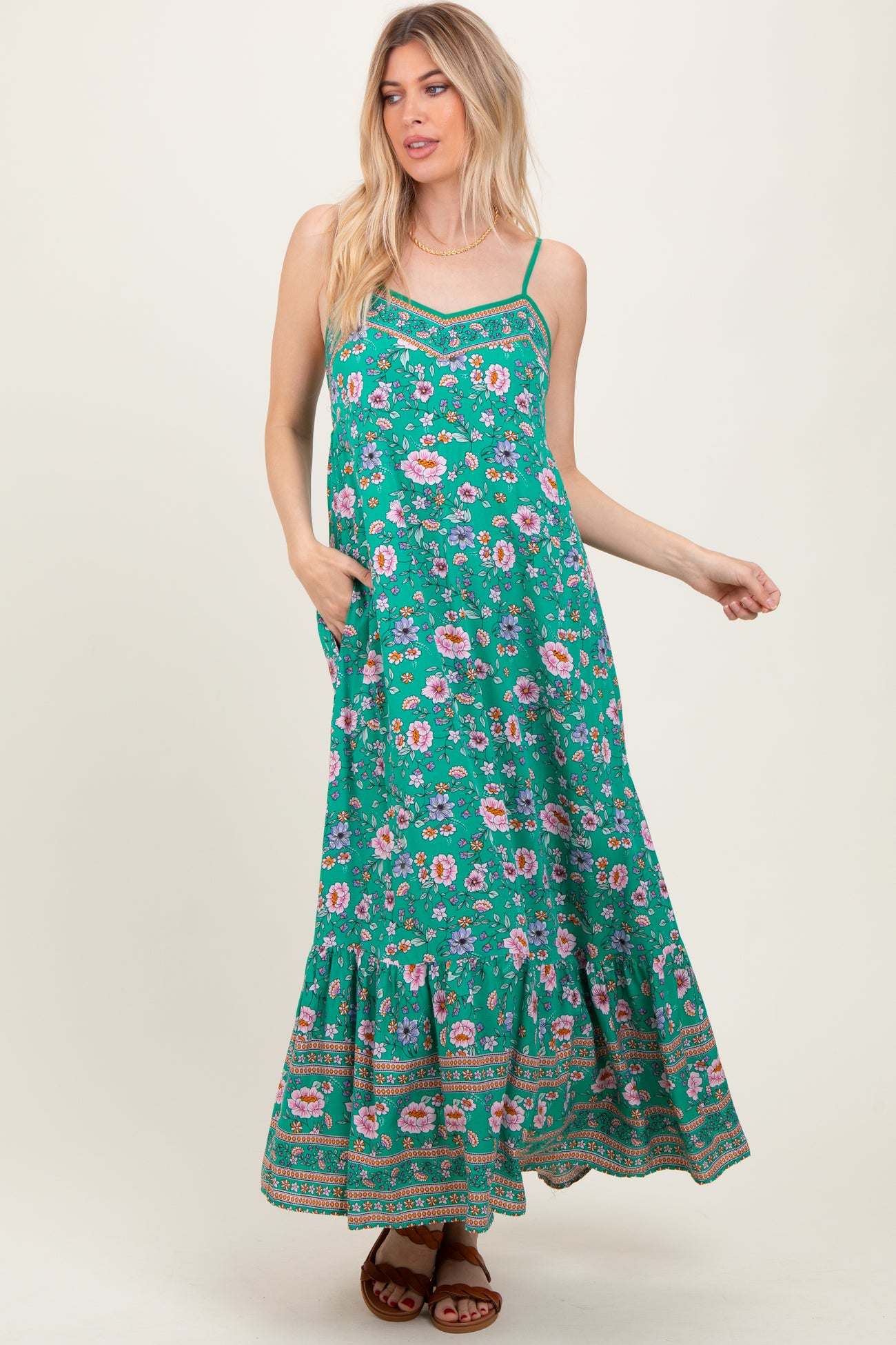 woman wearing a green maxi dress with floral print and spaghetti straps, featuring a tiered hem and pockets