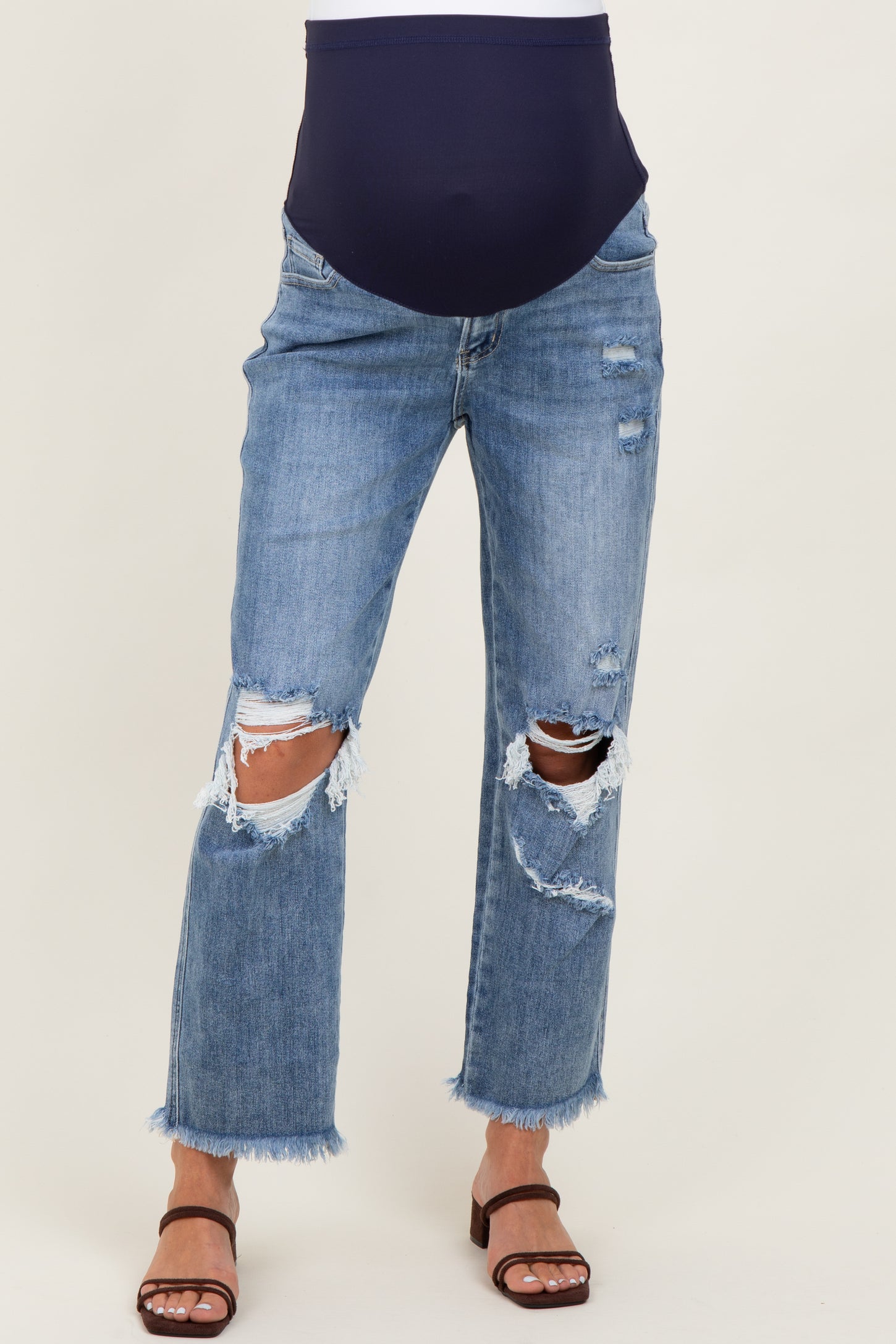 woman wearing light blue distressed maternity jeans with a navy band, featuring ripped details and frayed hems