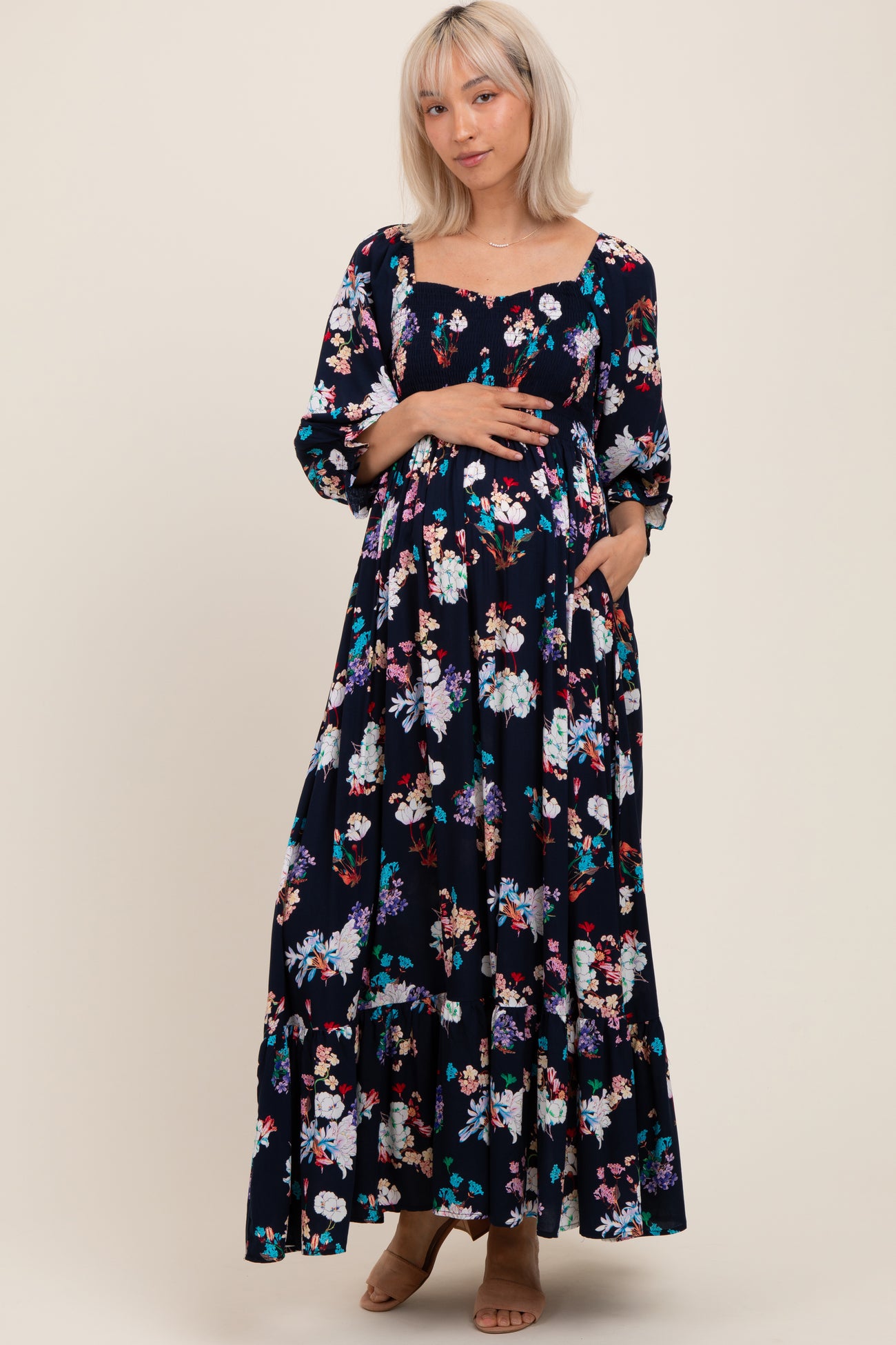 woman wearing a black floral print maternity maxi dress with long sleeves and pockets, showing her baby bump