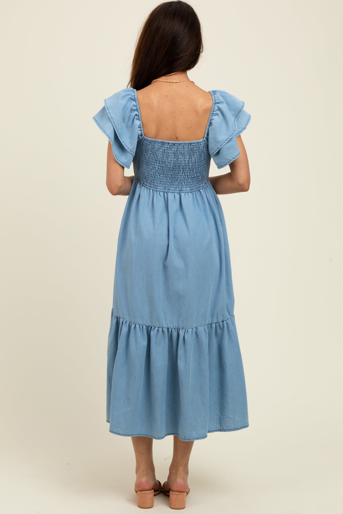 woman wearing a blue chambray maxi dress with ruffle sleeves and a smocked bodice, shown from the back