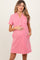 woman wearing a pink short sleeve maternity dress with a collar and pocket, cradling her baby bump