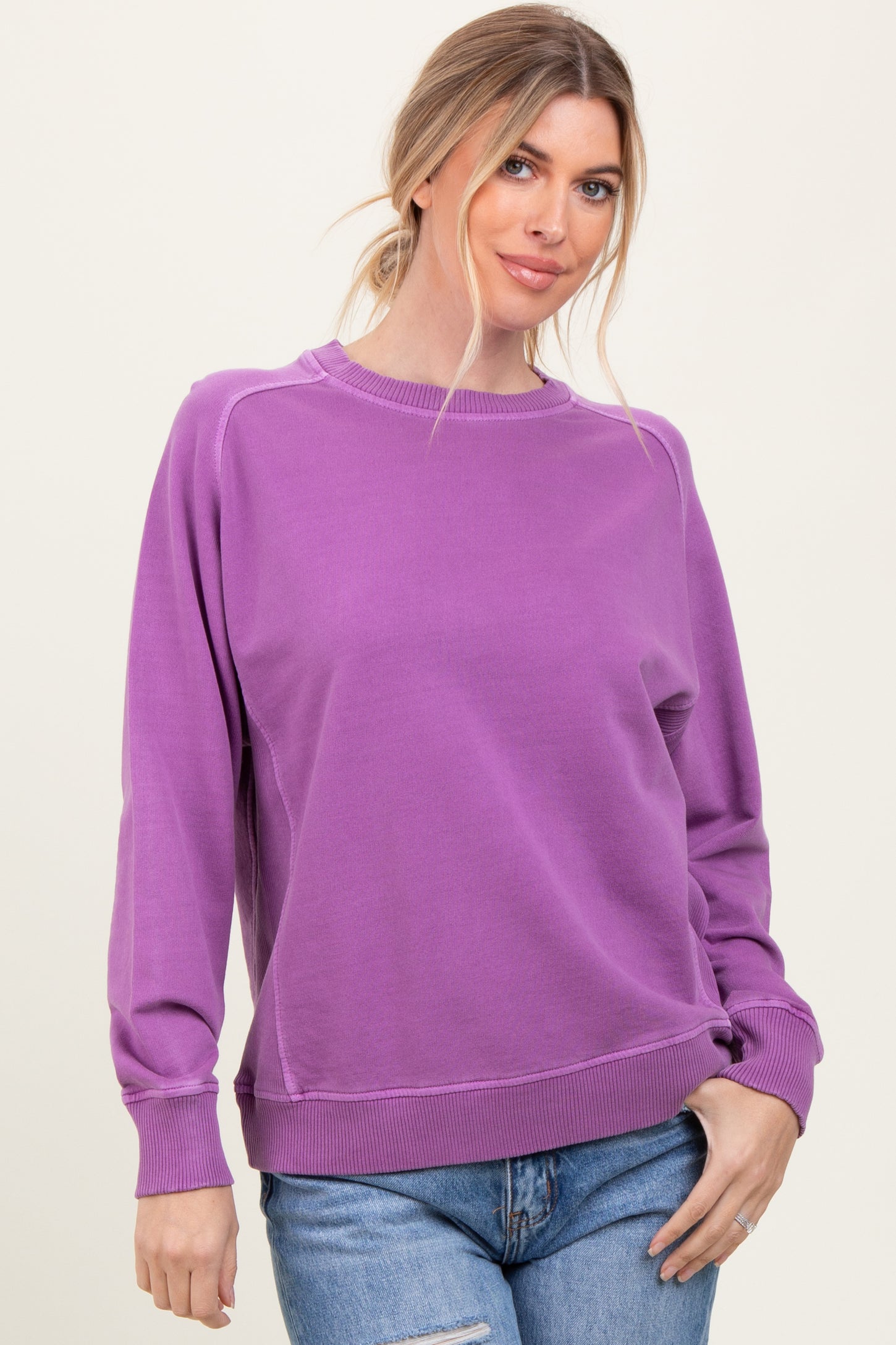 woman wearing a purple oversized sweatshirt with a crew neckline and ribbed cuffs, paired with blue jeans