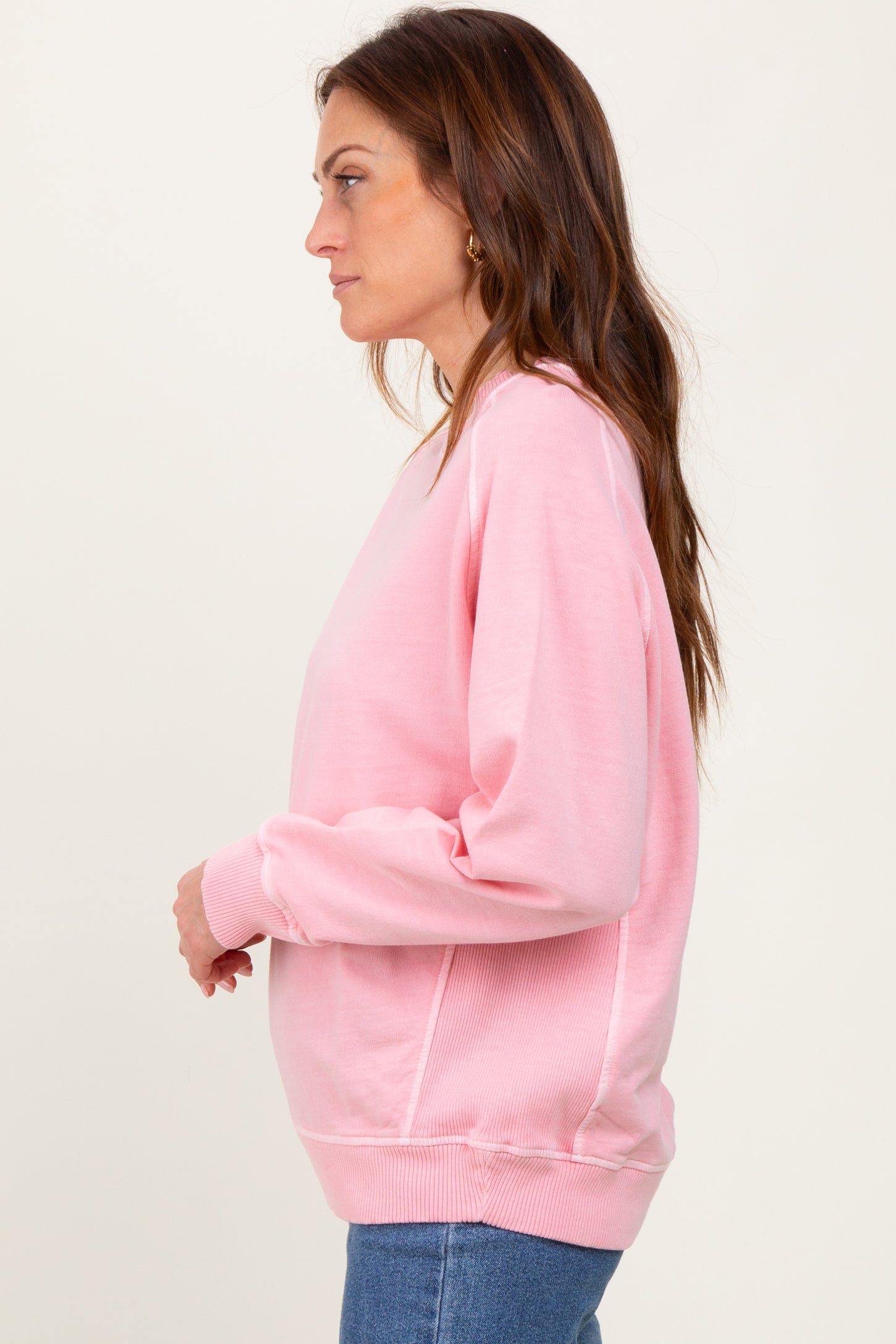 woman wearing a pink long sleeve sweatshirt with a relaxed fit and ribbed cuffs, styled with blue jeans