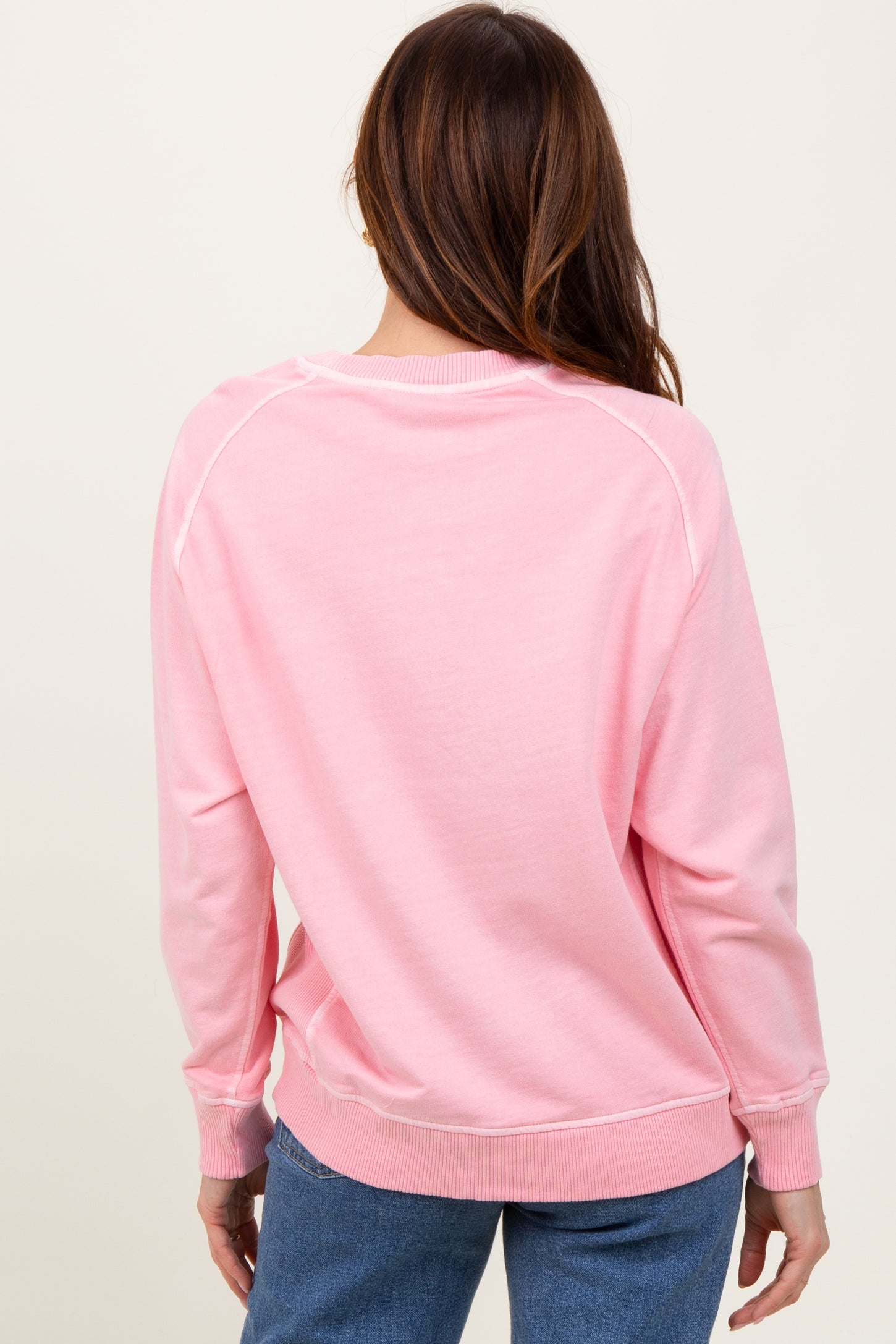 woman wearing a pink oversized sweatshirt with raglan sleeves and ribbed cuffs, viewed from the back