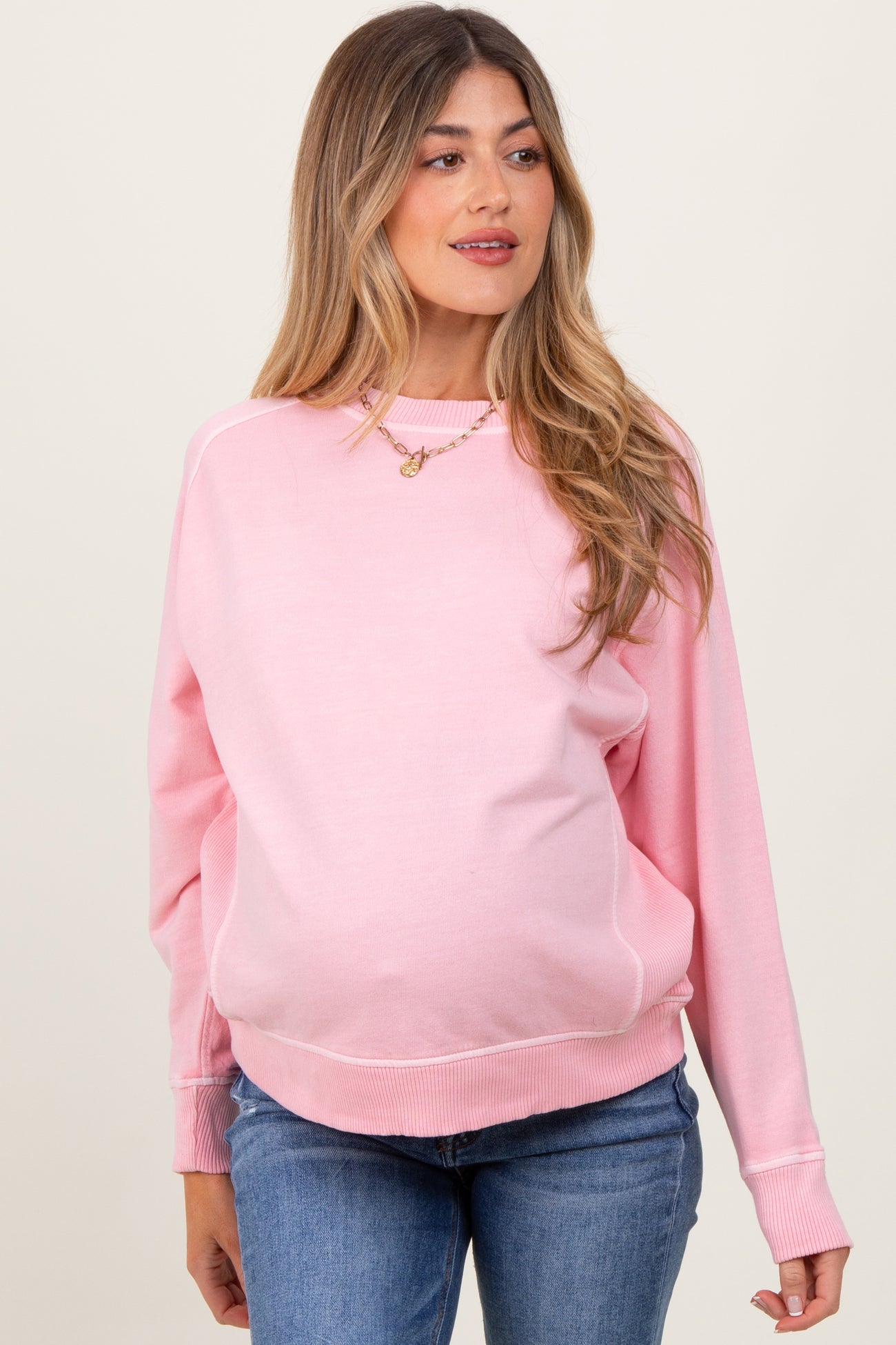 woman wearing a light pink maternity sweatshirt with a relaxed fit and visible baby bump