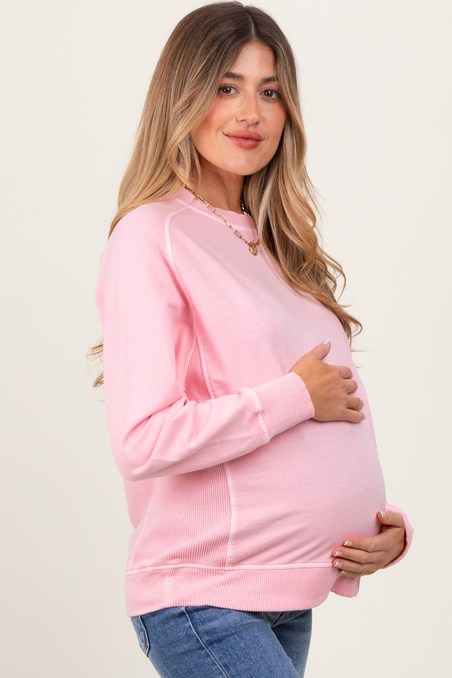 woman wearing a pink maternity sweatshirt with a visible baby bump and holding her belly