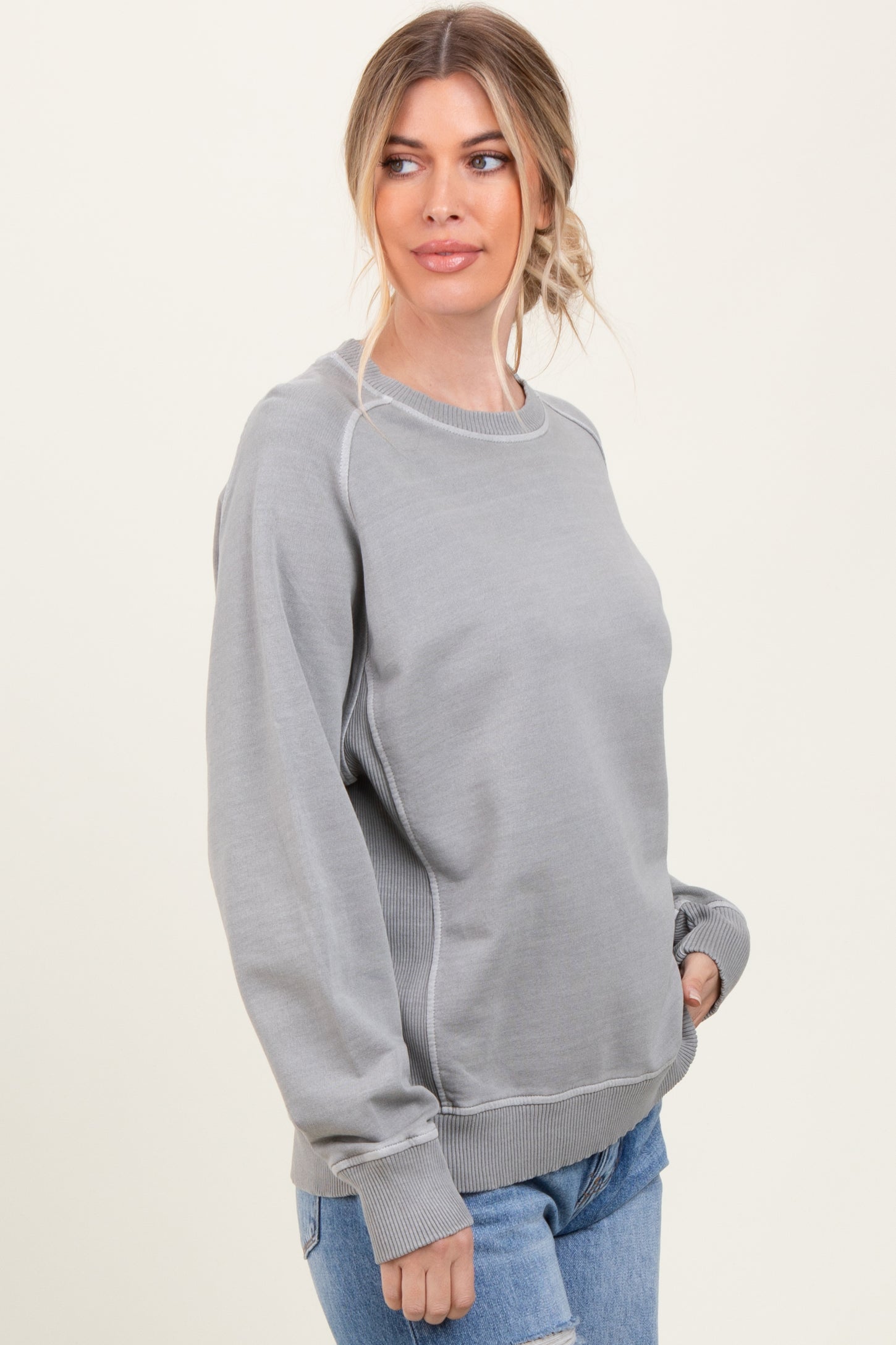 woman wearing a gray crew neck sweatshirt with ribbed cuffs and waistband, styled with light blue jeans