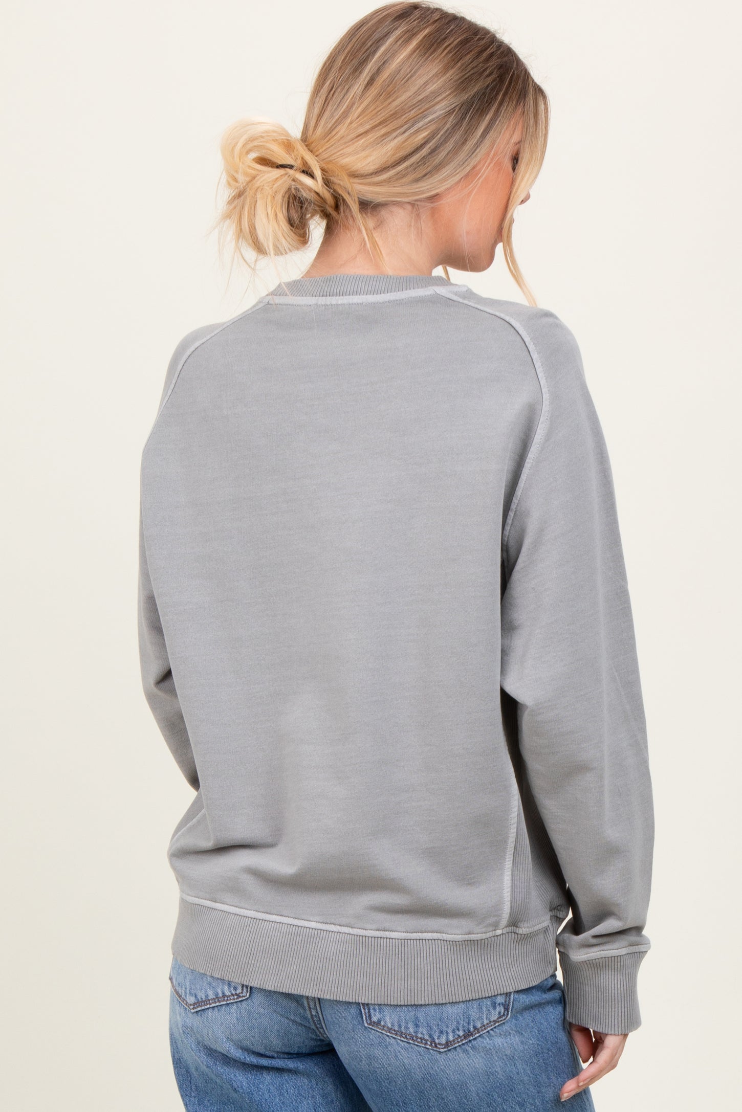 woman wearing a grey long sleeve sweatshirt with a relaxed fit and ribbed cuffs, viewed from the back
