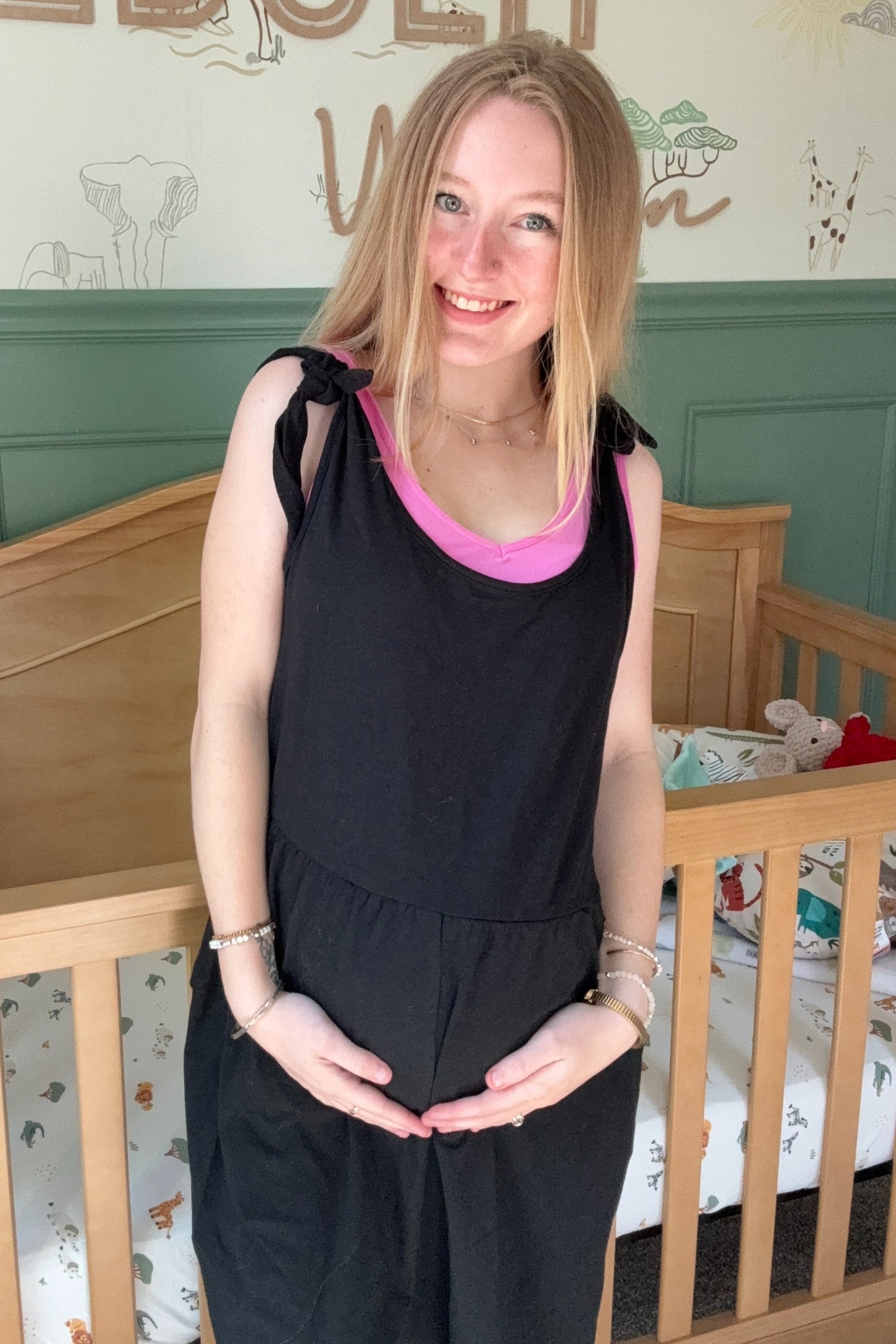 woman wearing a black maternity dress with tie straps and a pink tank top, holding her baby bump
