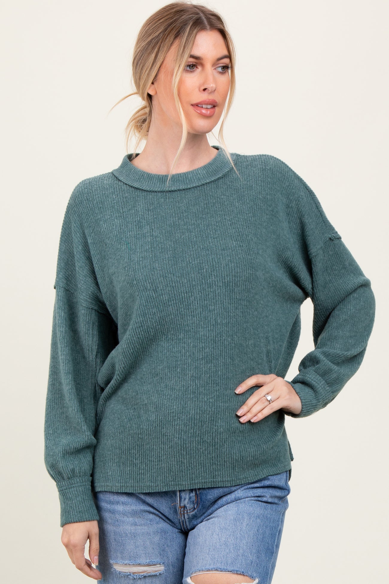 woman wearing a green ribbed long sleeve sweater with a relaxed fit and oversized cuffs, paired with distressed denim shorts