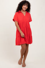 woman wearing a red tiered short sleeve dress with a collar and frayed hem, standing with one hand on her dress
