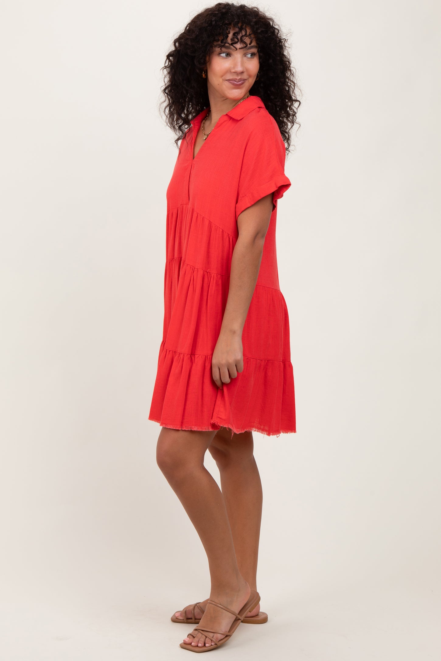 woman wearing a red short sleeve tiered dress with a collar and frayed hem, standing sideways
