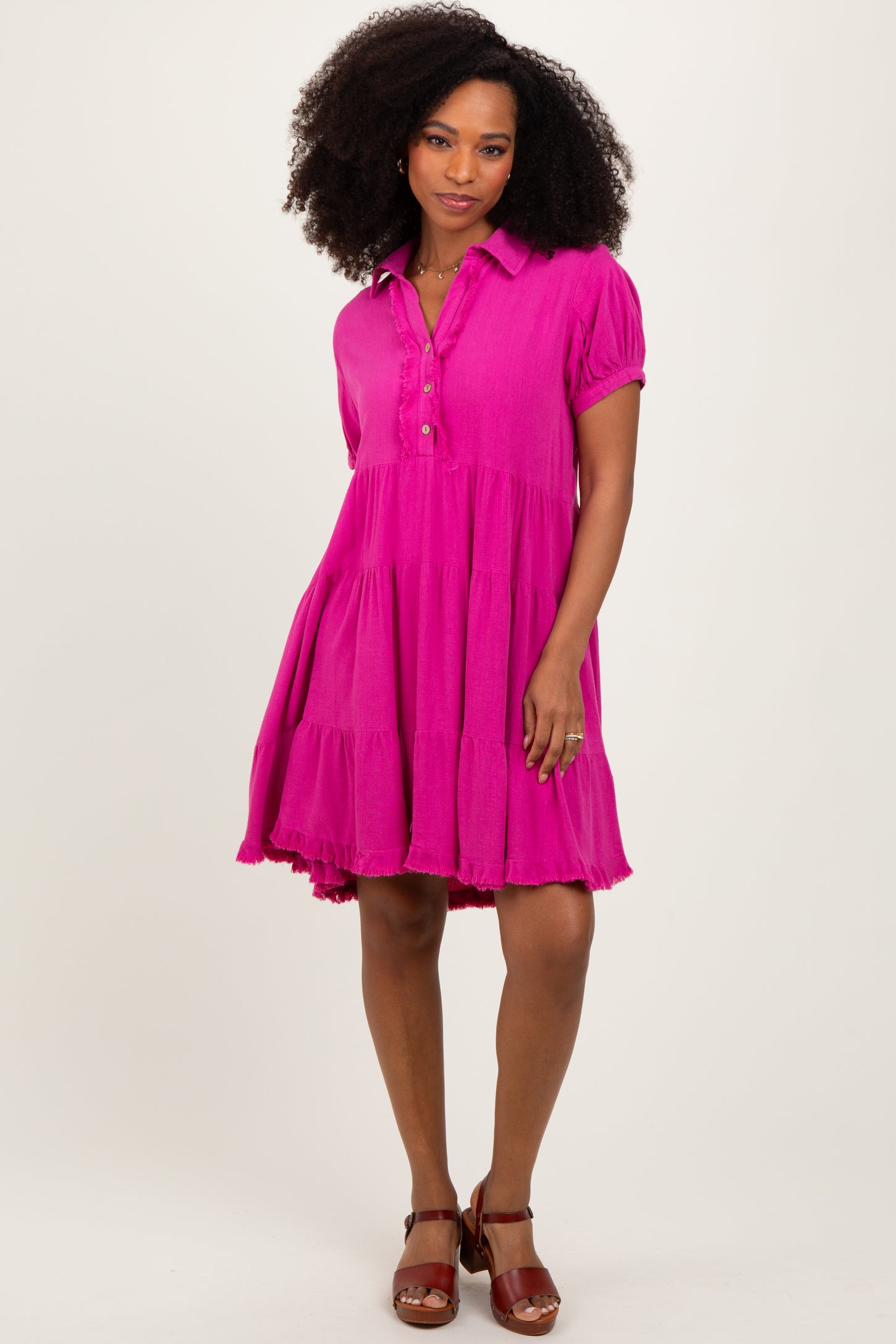 woman wearing a bright pink short sleeve tiered dress with a button-down collar and a flared silhouette