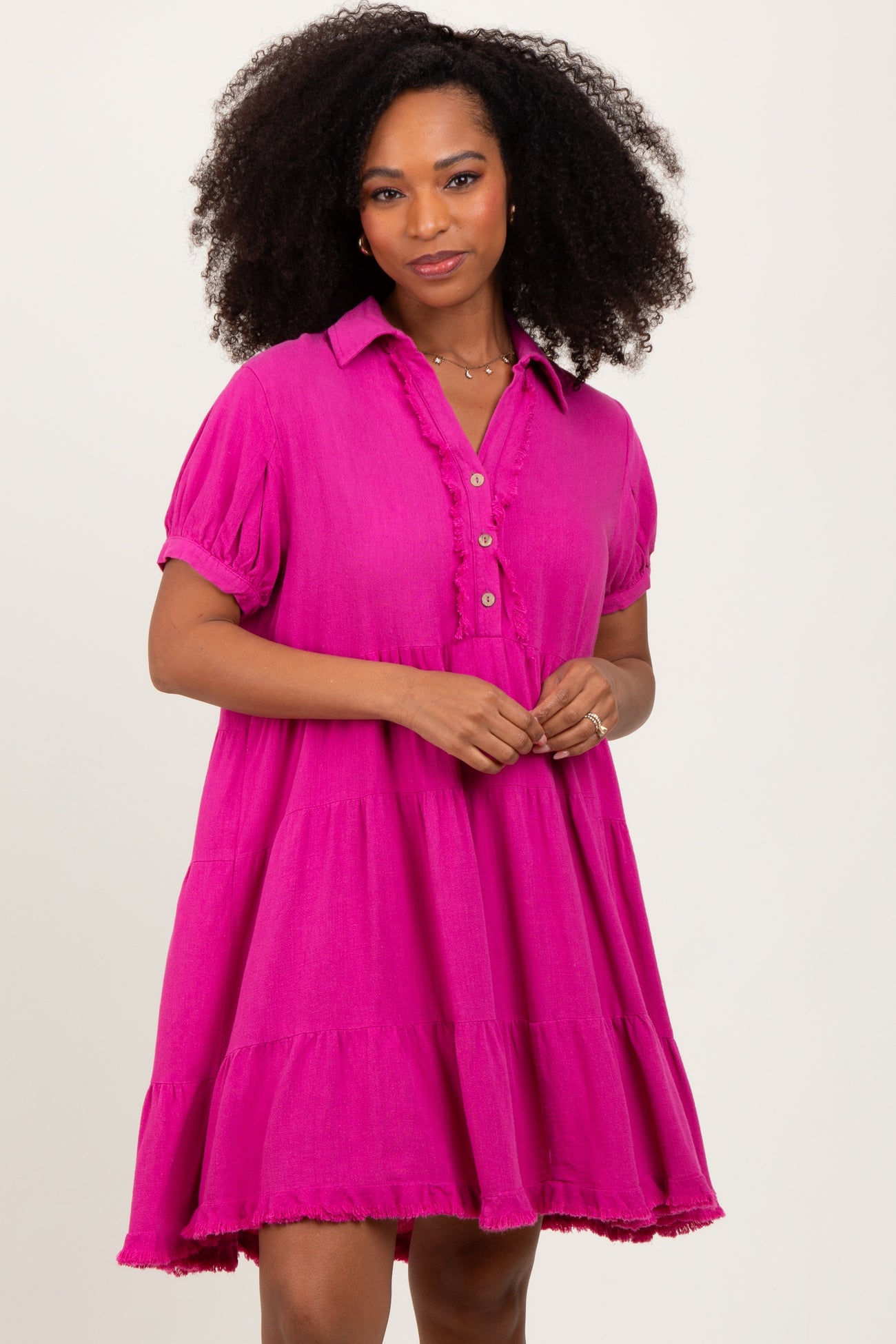 woman wearing a bright pink short sleeve dress with a collar, button-up front, and tiered skirt details