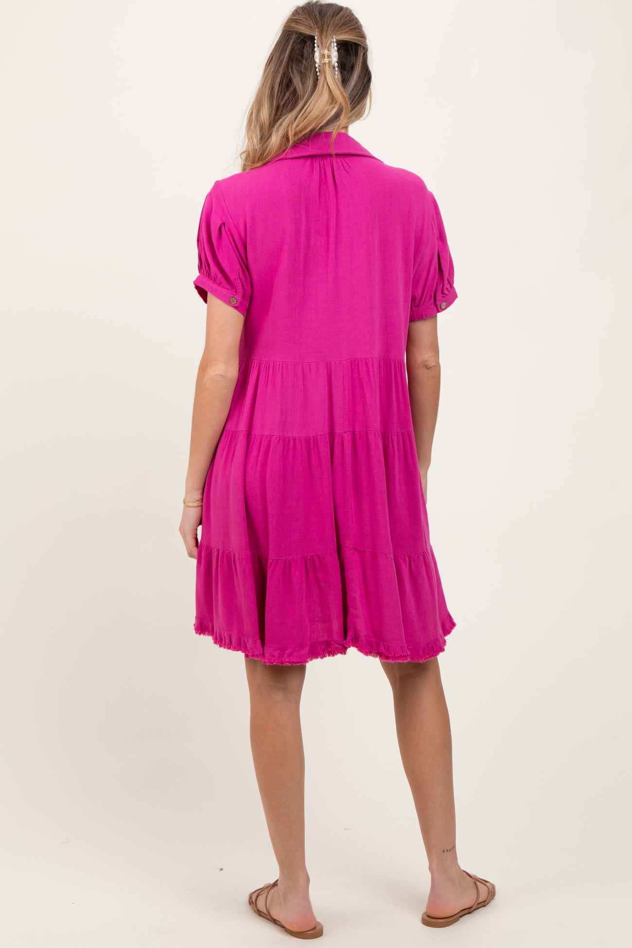woman wearing a vibrant pink short sleeve maternity dress with a tiered hem, showing her baby bump from the back