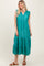 woman wearing a teal maxi dress with ruffle details and a tied neckline, standing against a light background