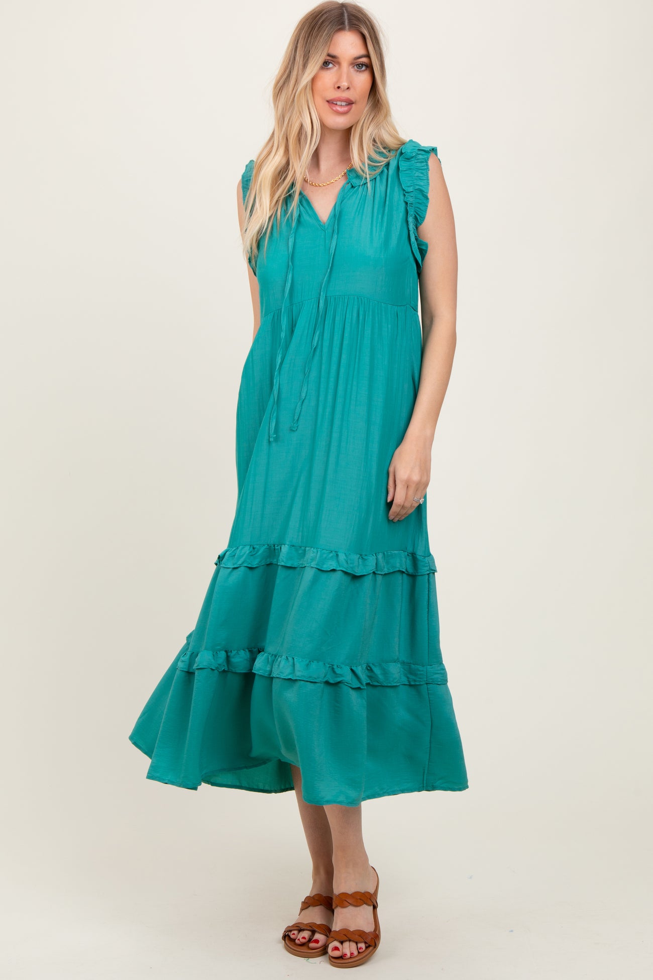 woman wearing a turquoise midi dress with ruffle details and a tie neck, standing against a neutral background