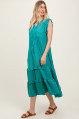 woman wearing a teal maxi dress with ruffle details and tie neck, standing against a plain background
