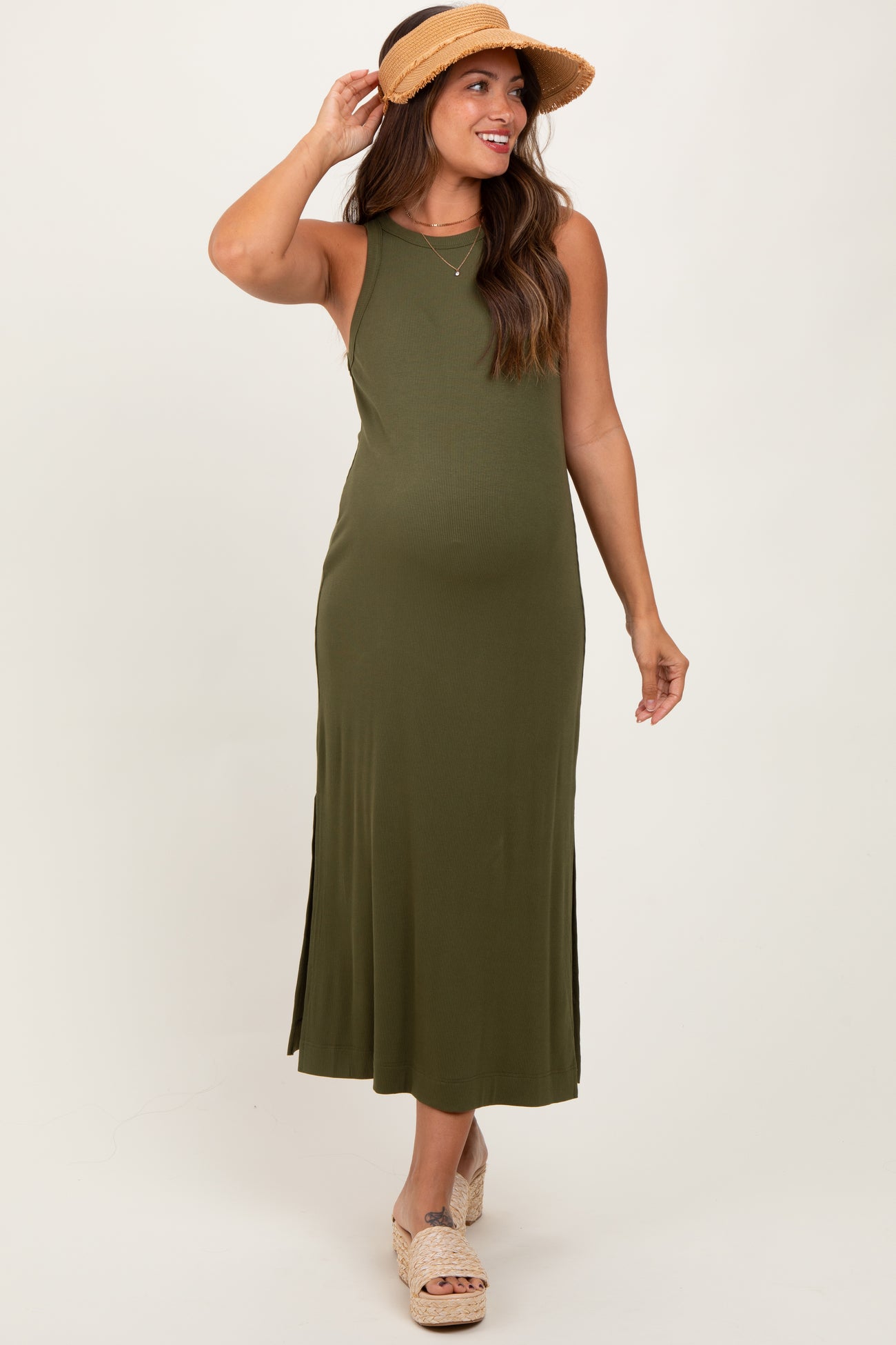 woman wearing an olive green maternity maxi dress with side slits and a sun hat, showcasing her baby bump