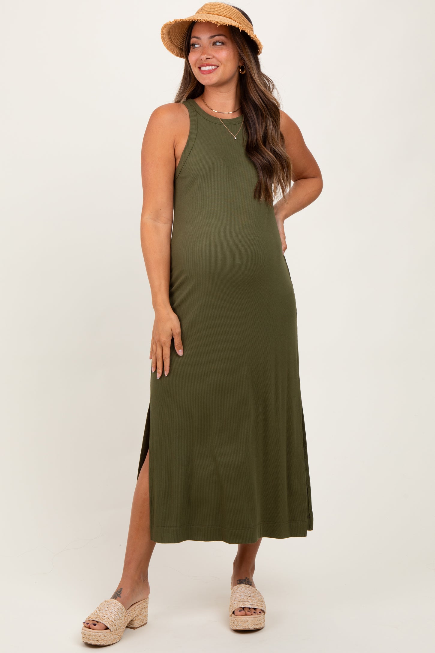 woman wearing an olive green maternity maxi dress with side slits and a straw hat, showing her baby bump