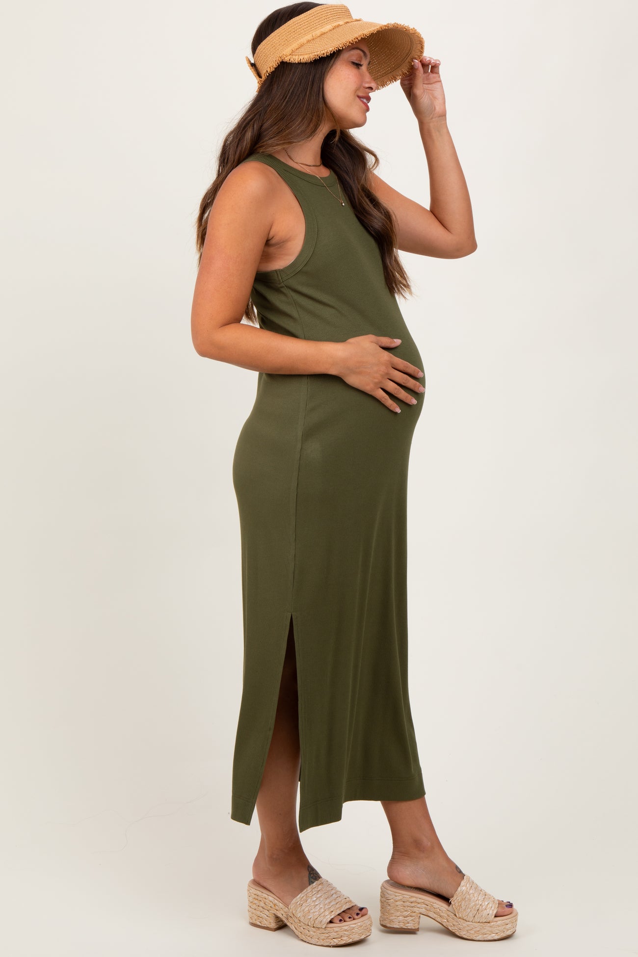 woman wearing a dark green maternity maxi dress with side slits, gently holding her baby bump outdoors