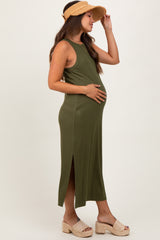 woman wearing a dark green maternity maxi dress with side slits, gently holding her baby bump outdoors