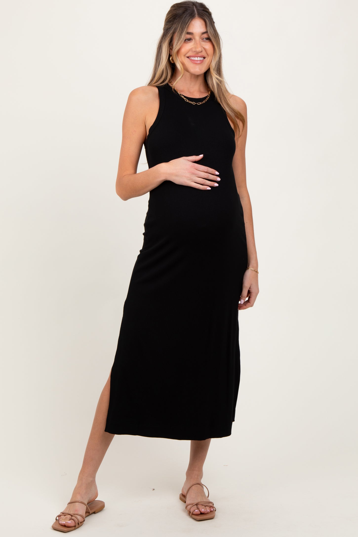 woman wearing a black ribbed maternity maxi dress with side slits and holding her baby bump