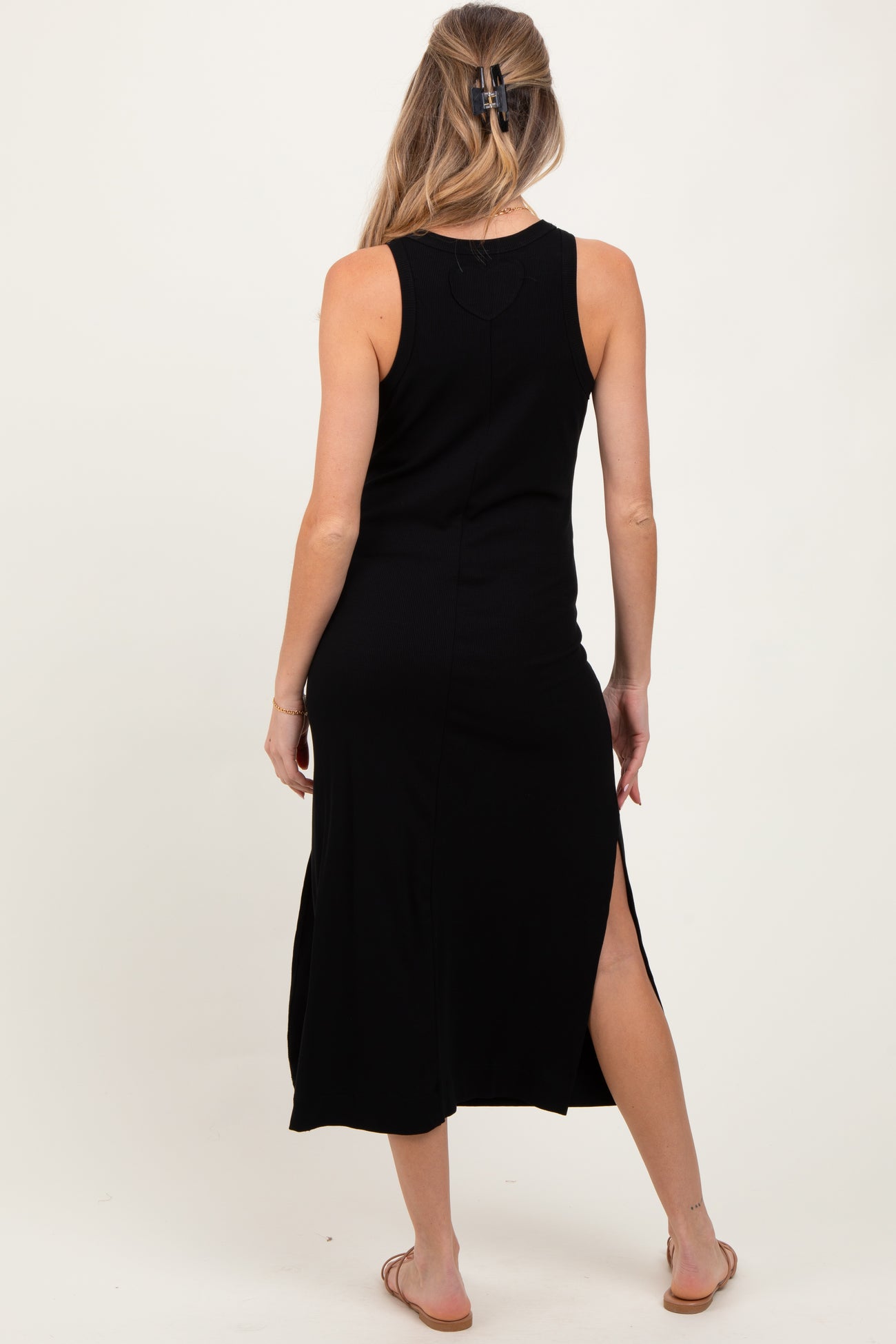 woman wearing a black sleeveless maternity dress with a side slit, showing her back and long hair