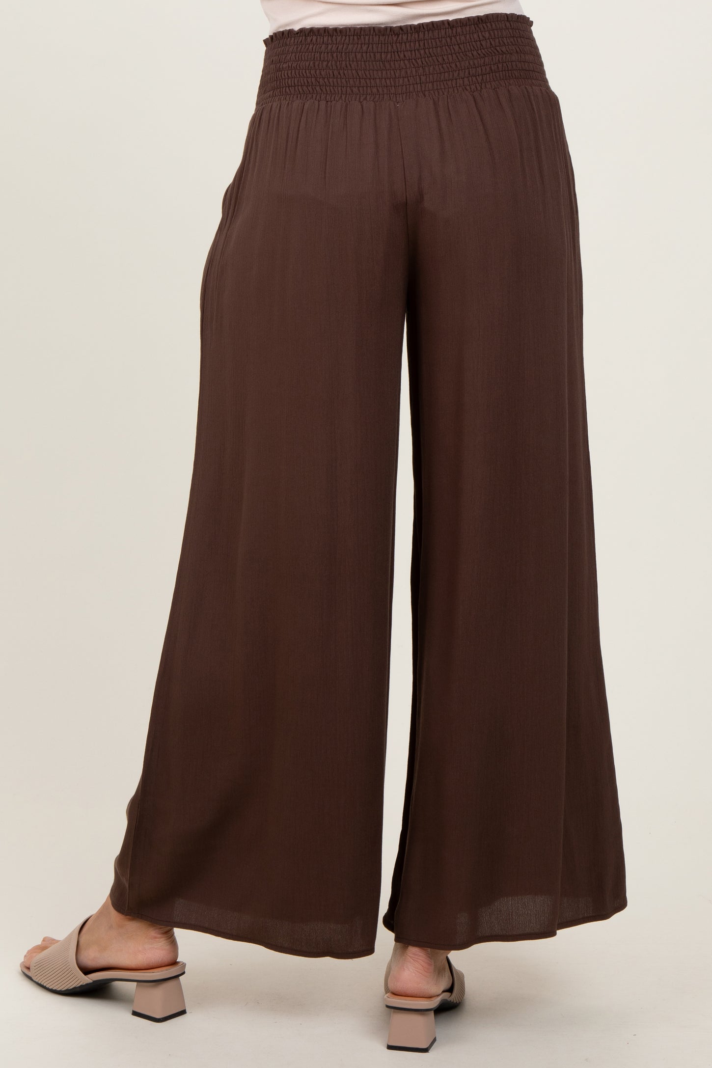 woman wearing brown wide-leg trousers with a smocked waistband, viewed from the back