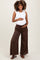 woman wearing a white ruffled maternity tank top and brown wide-leg maternity pants, holding her baby bump
