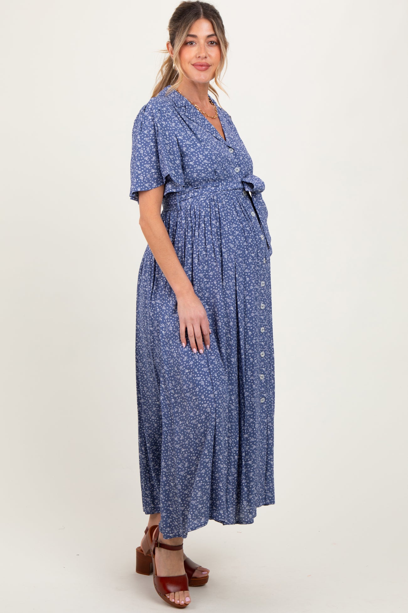 woman wearing a blue floral maternity maxi dress with a tie waist and buttons, showcasing her baby bump
