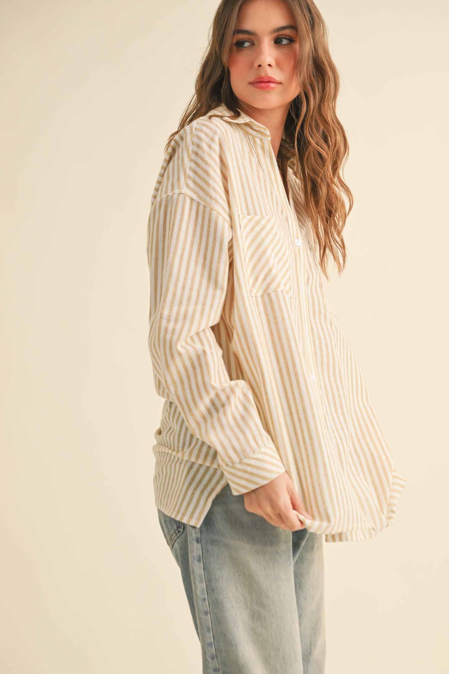 woman wearing a cream and beige striped oversized button-up shirt with a front pocket and loose-fitting jeans