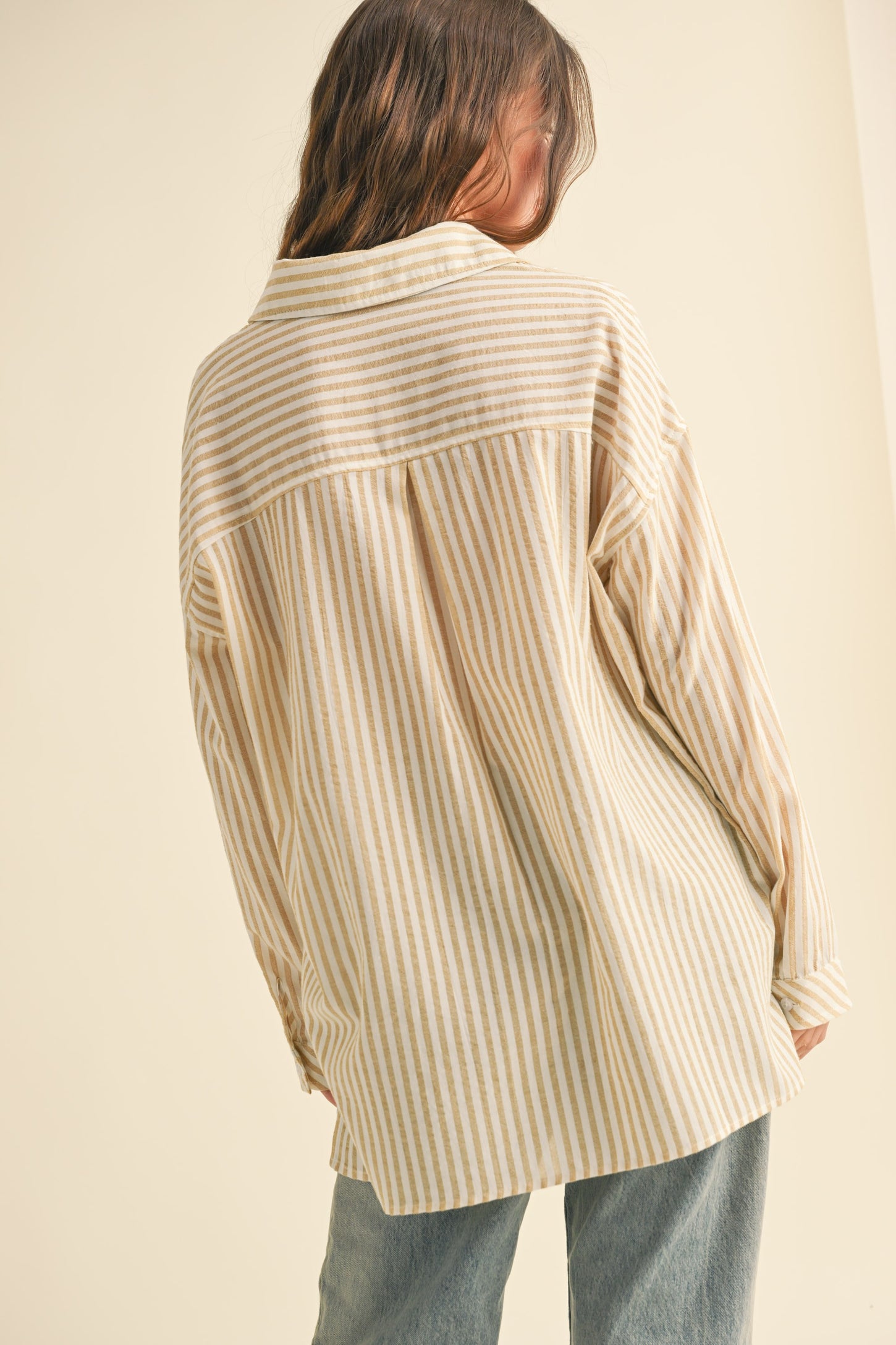 woman wearing a beige and white striped oversized button-up shirt, seen from the back, paired with light blue jeans