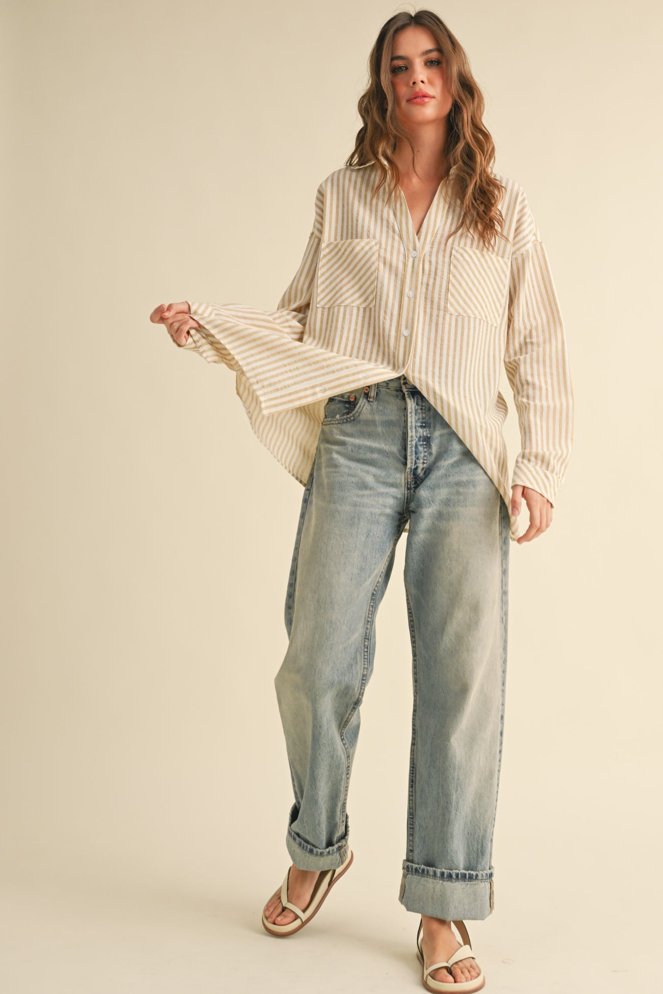 woman wearing a beige and white striped oversized button-up shirt with two front pockets and light wash baggy jeans
