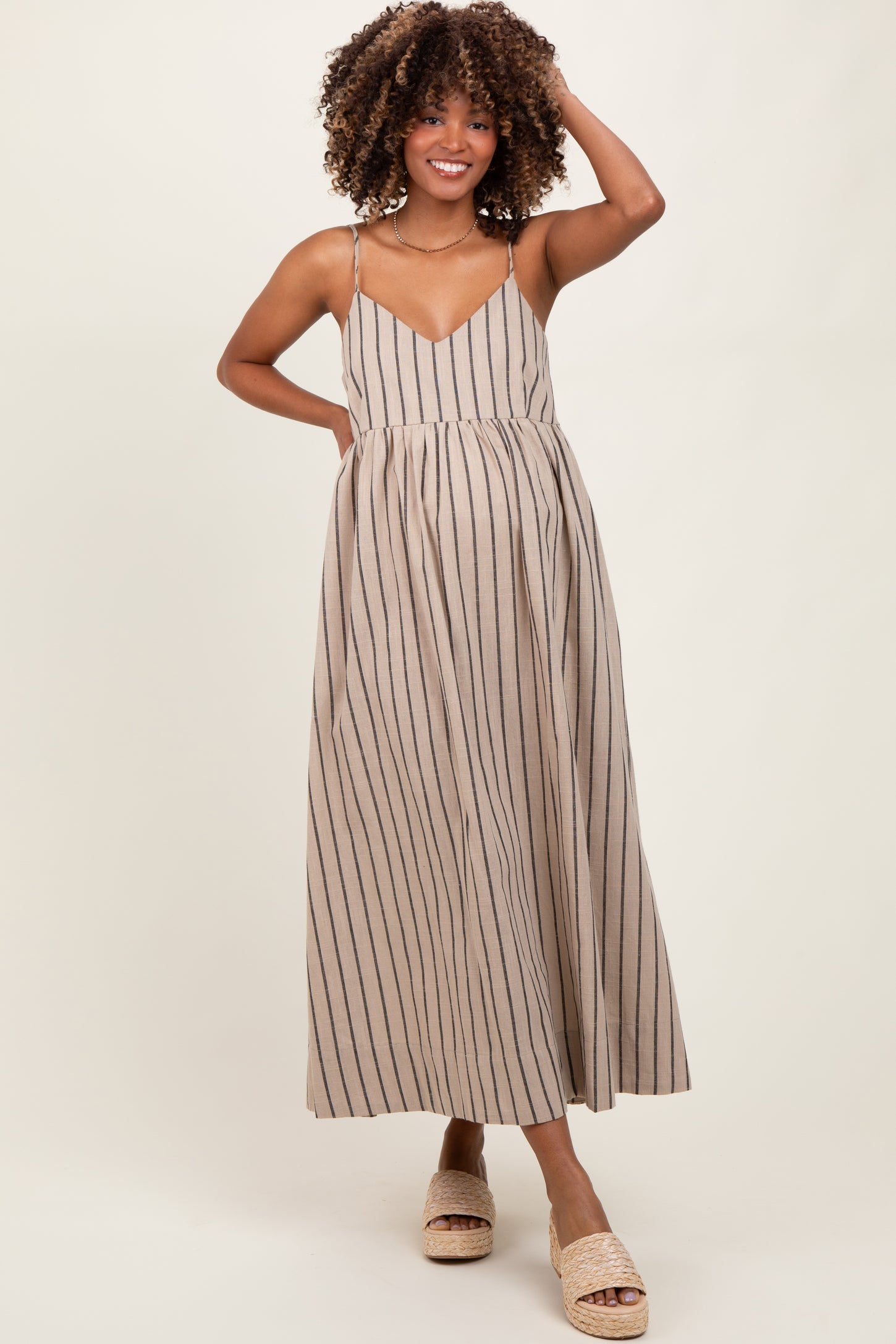 woman wearing a tan and navy striped maternity maxi dress with a flowy skirt and spaghetti straps, showing her baby bump