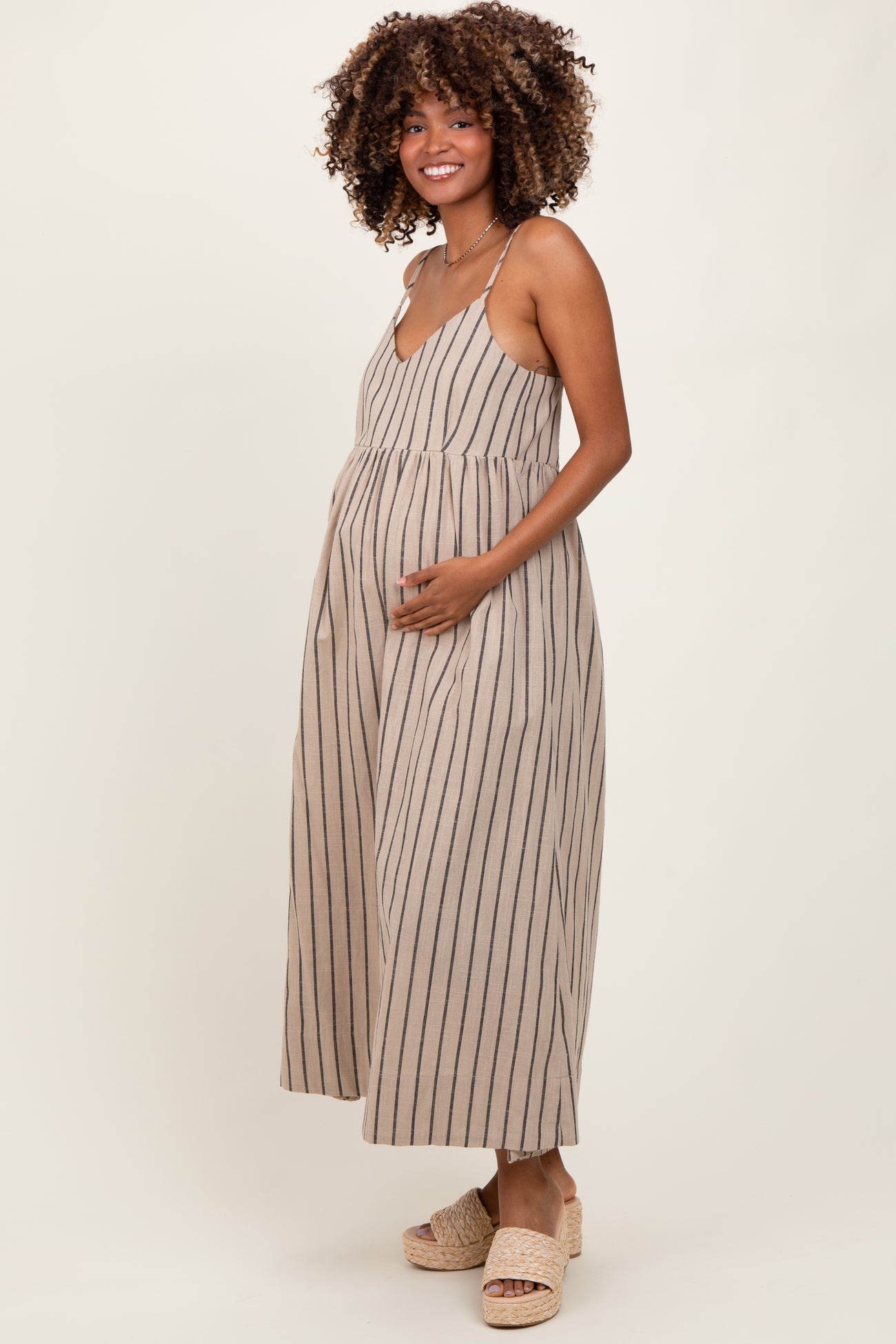 woman wearing a beige striped maternity dress with a v-neck and holding her baby bump