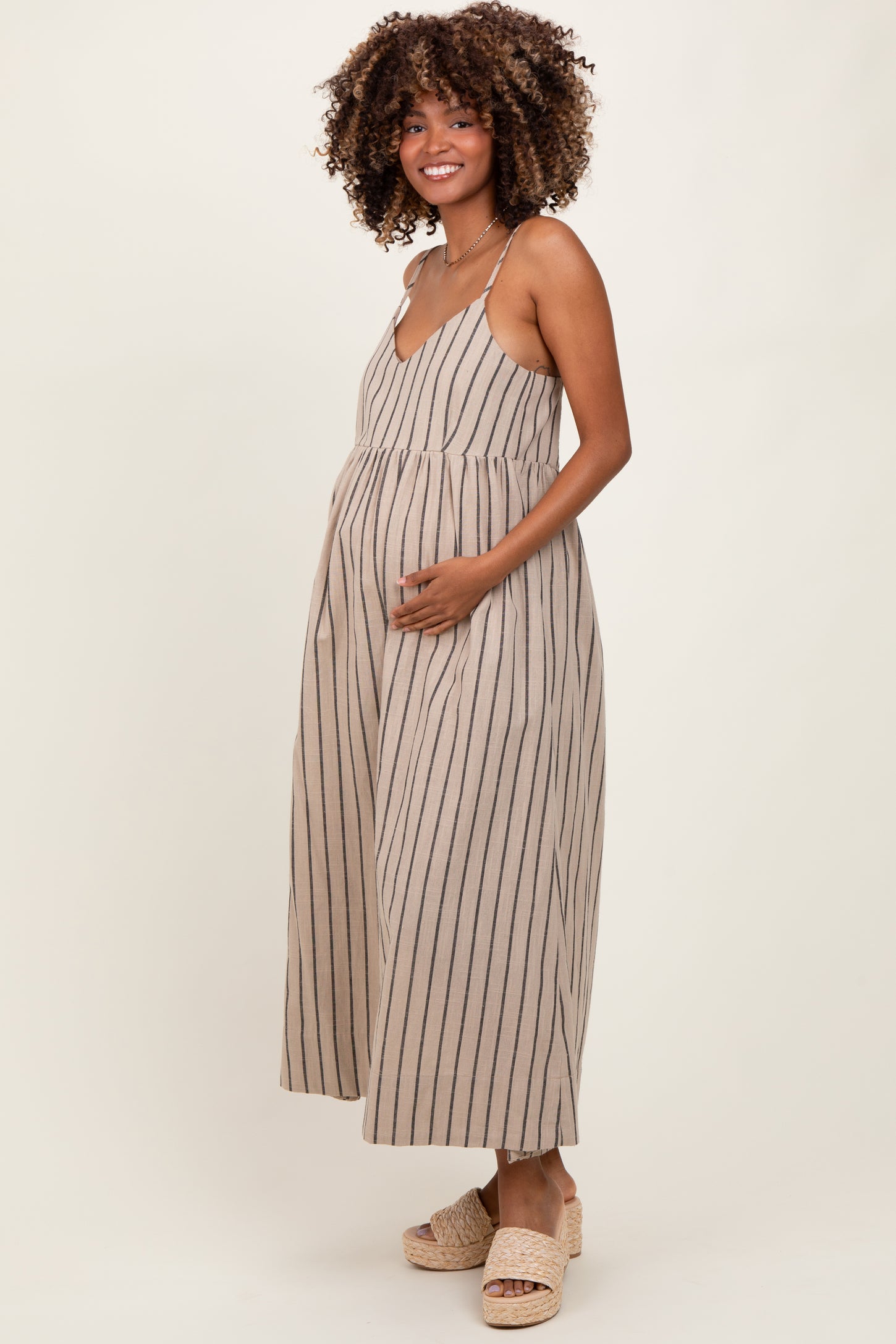 woman wearing a beige striped maternity dress with a v-neck and holding her baby bump