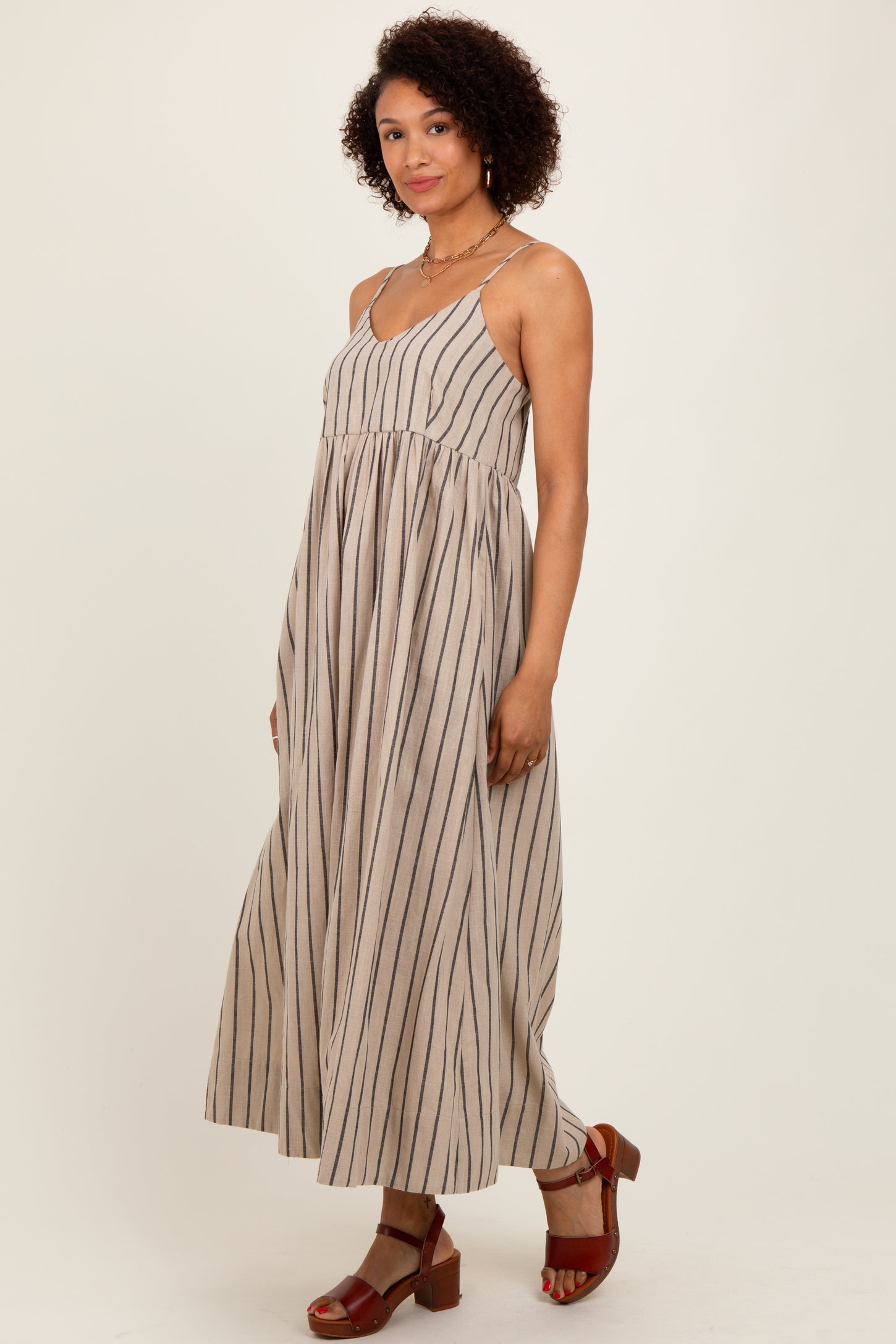 woman wearing a light brown striped maxi dress with a fitted bodice and flowy skirt, paired with brown sandals