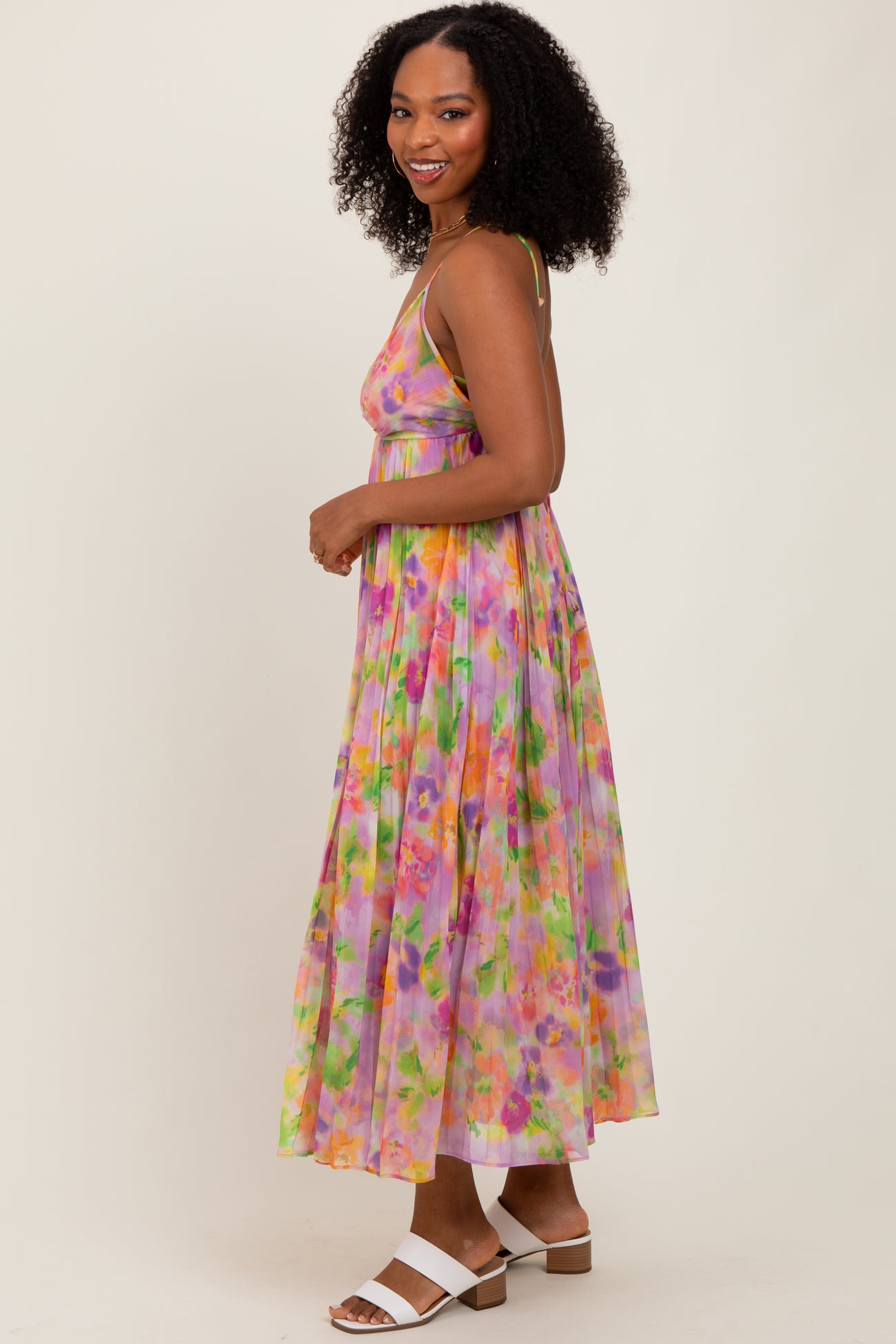 woman wearing a colorful floral maxi dress with a flowy design and spaghetti straps, smiling while standing sideways