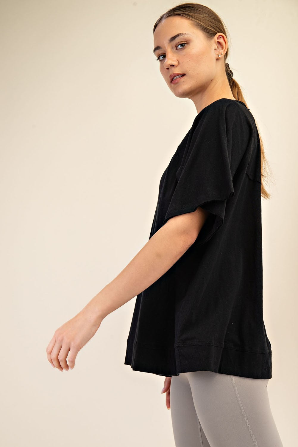 woman wearing a black oversized short sleeve top with relaxed fit and side slits, paired with grey leggings