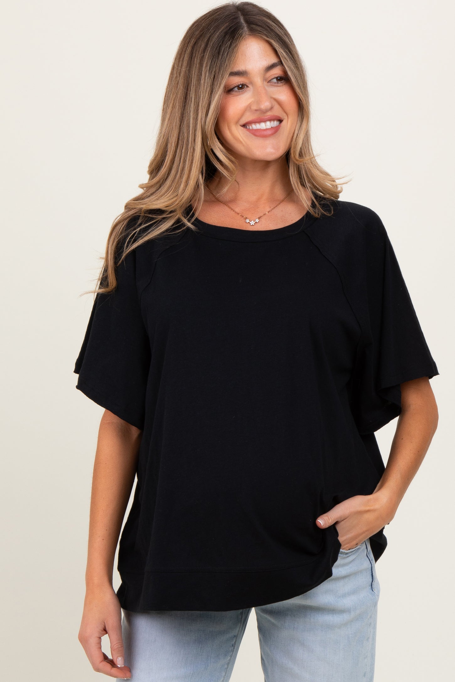 woman wearing a black maternity top with short sleeves and a relaxed fit, smiling and posing with one hand in her pocket