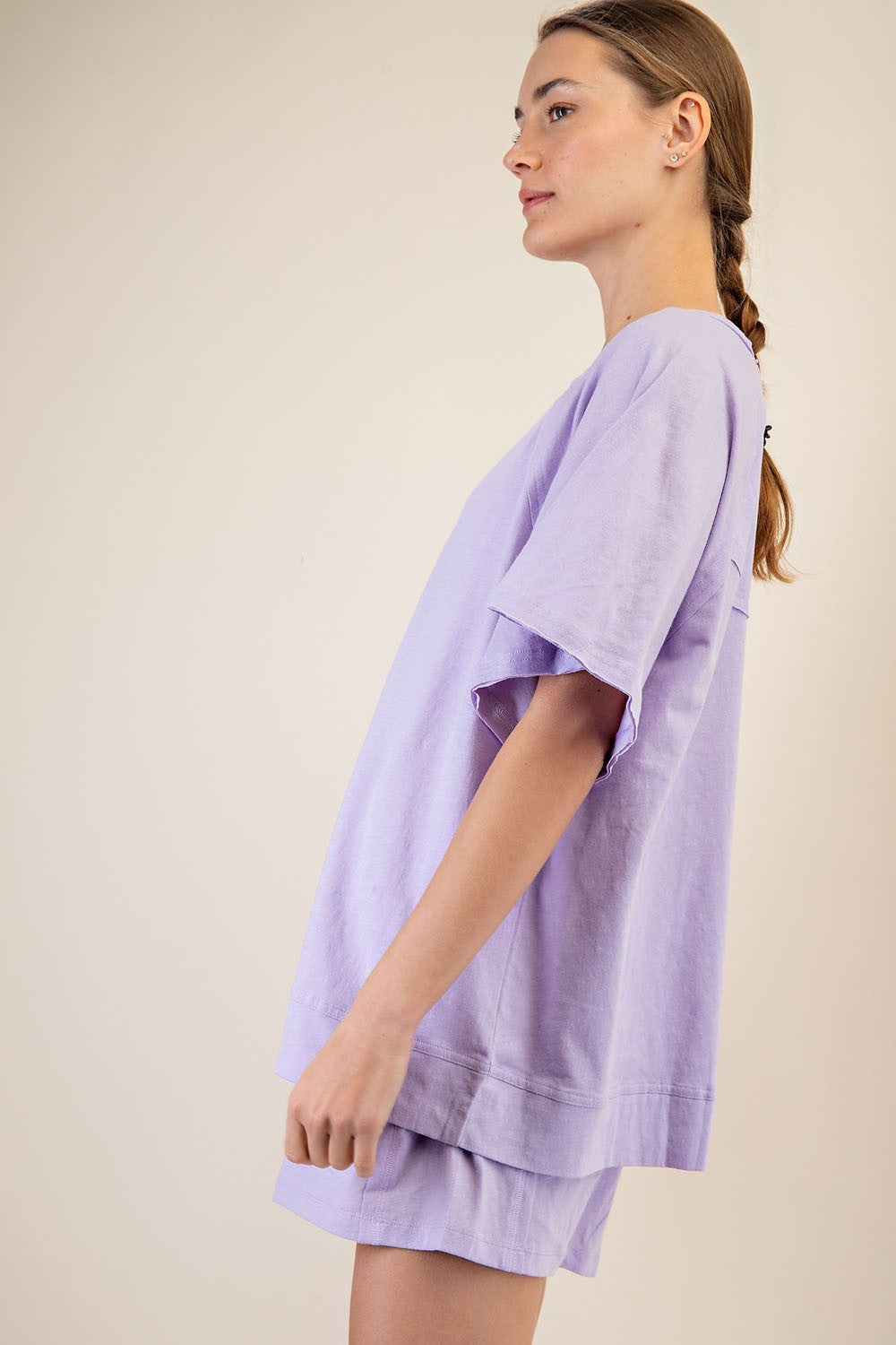 woman wearing a lilac oversized t-shirt with side slits and matching shorts, standing sideways against a neutral background