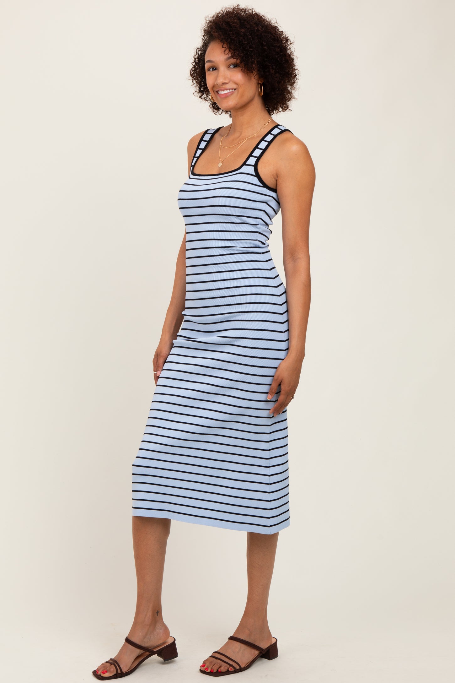 woman wearing a blue and white striped sleeveless midi dress with a fitted silhouette and button details on the straps