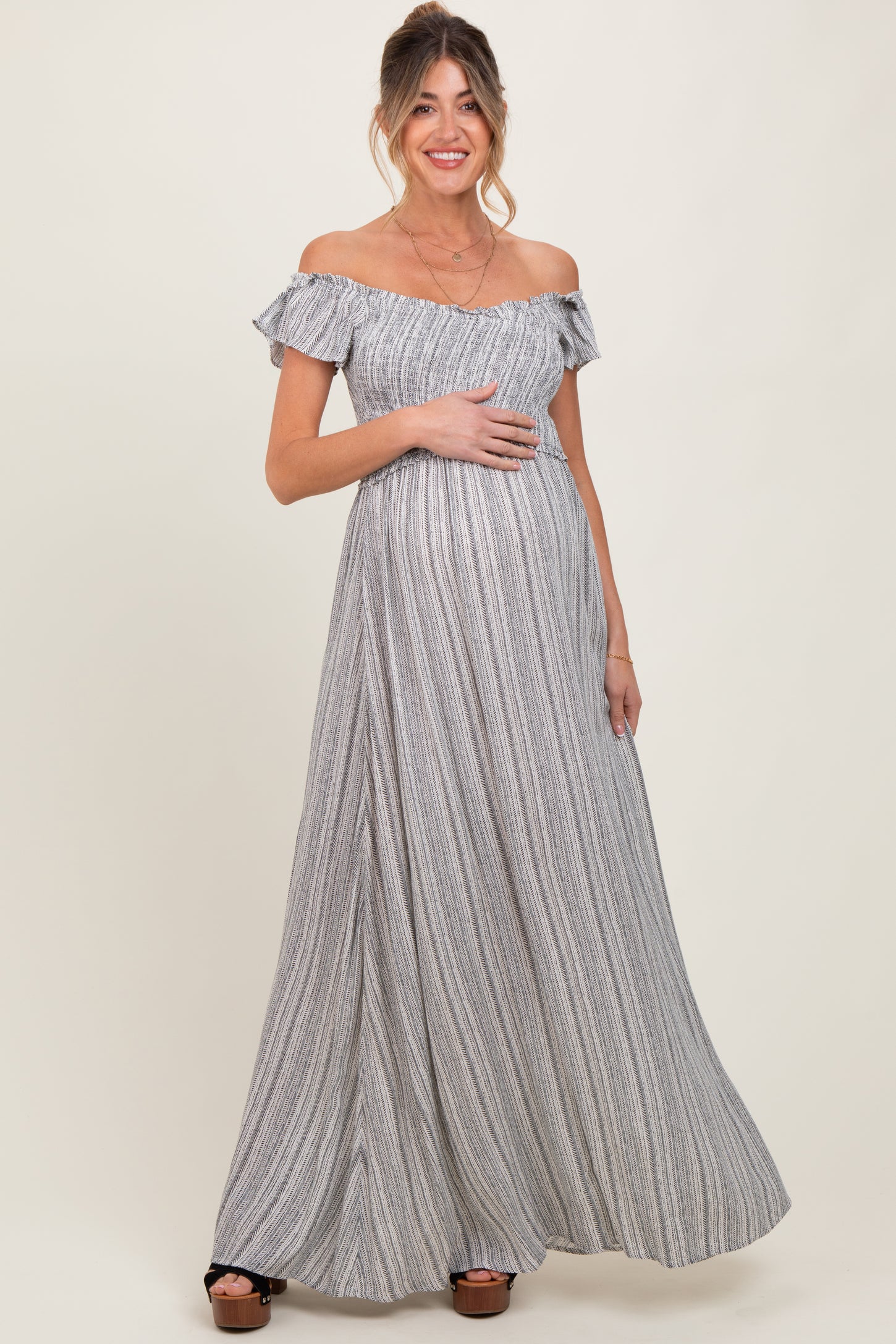 woman wearing a striped off-shoulder maxi maternity dress and showing her baby bump
