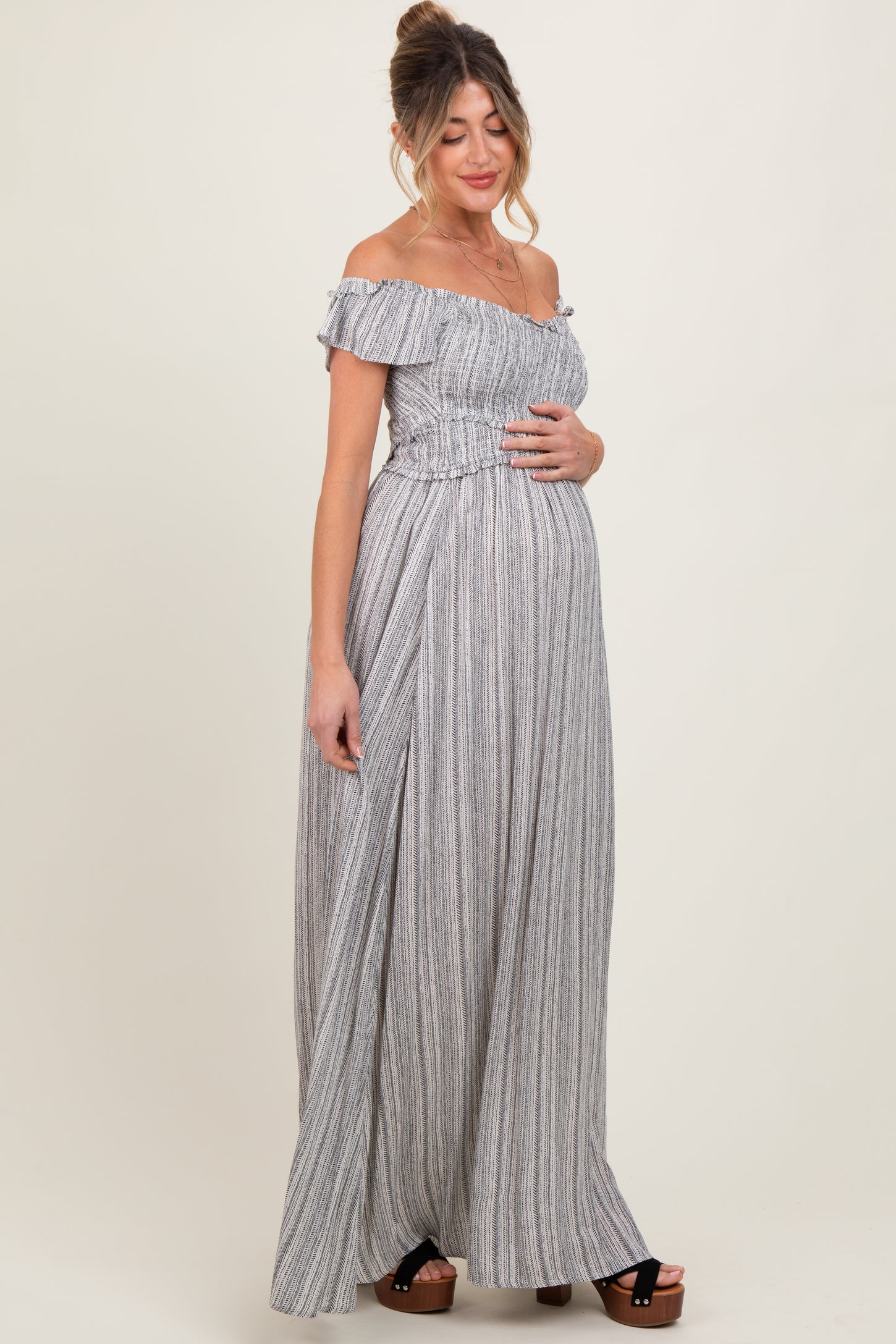woman wearing a striped off-the-shoulder maternity maxi dress and gently holding her baby bump