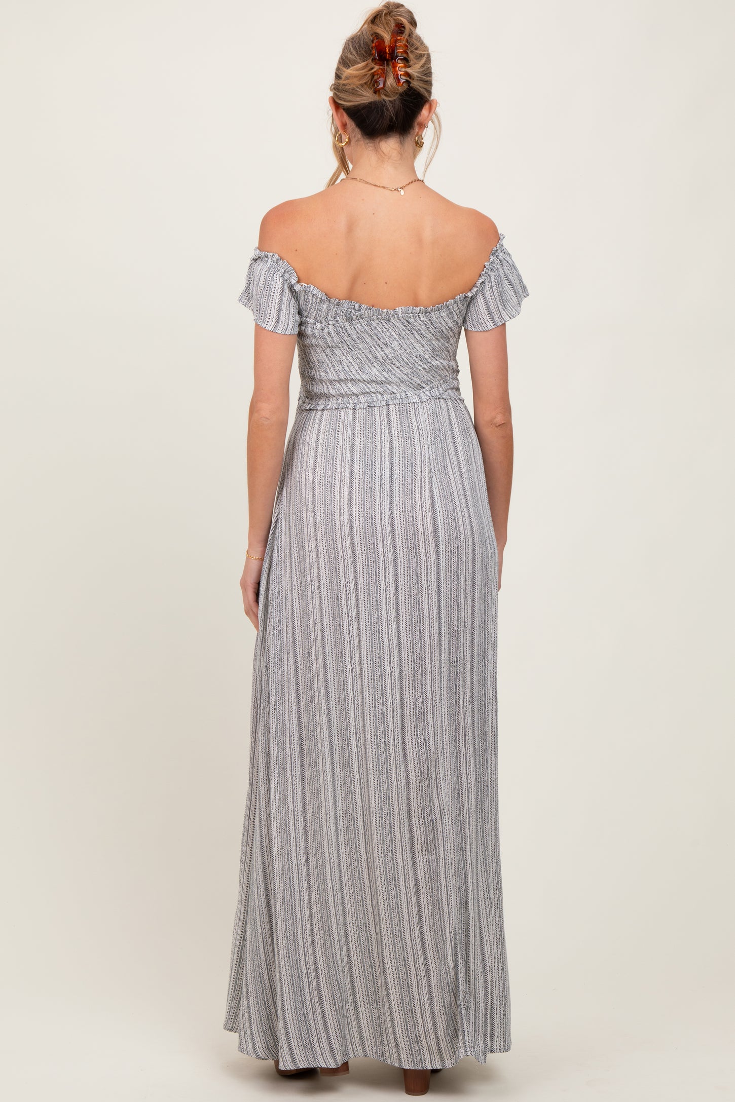 woman wearing a striped off-the-shoulder maxi maternity dress, showing the back view and flowing skirt